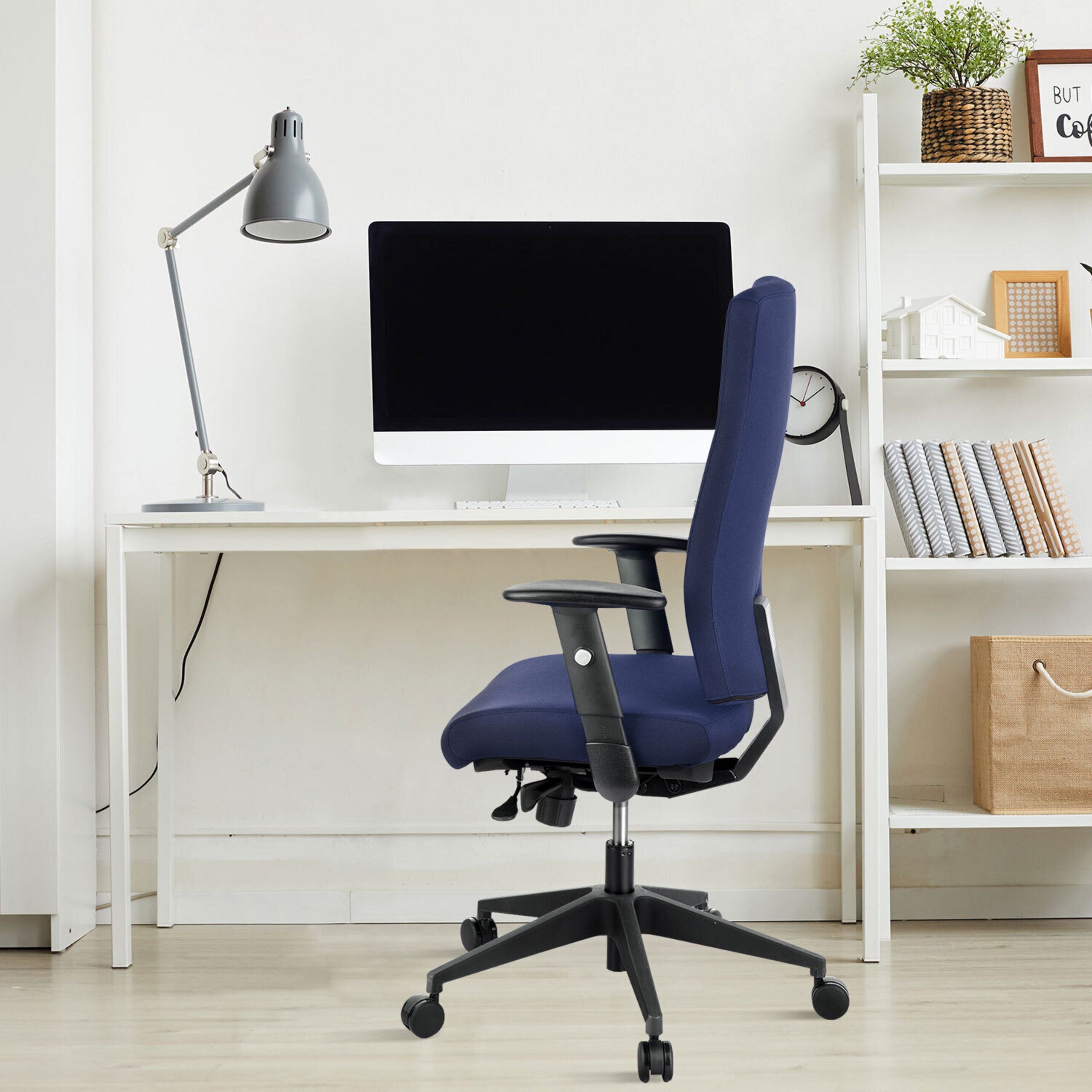 Ein blauer Bürostuhl steht an einem weißen Schreibtisch mit Computer und Lampe, neben einem weißen Regal.