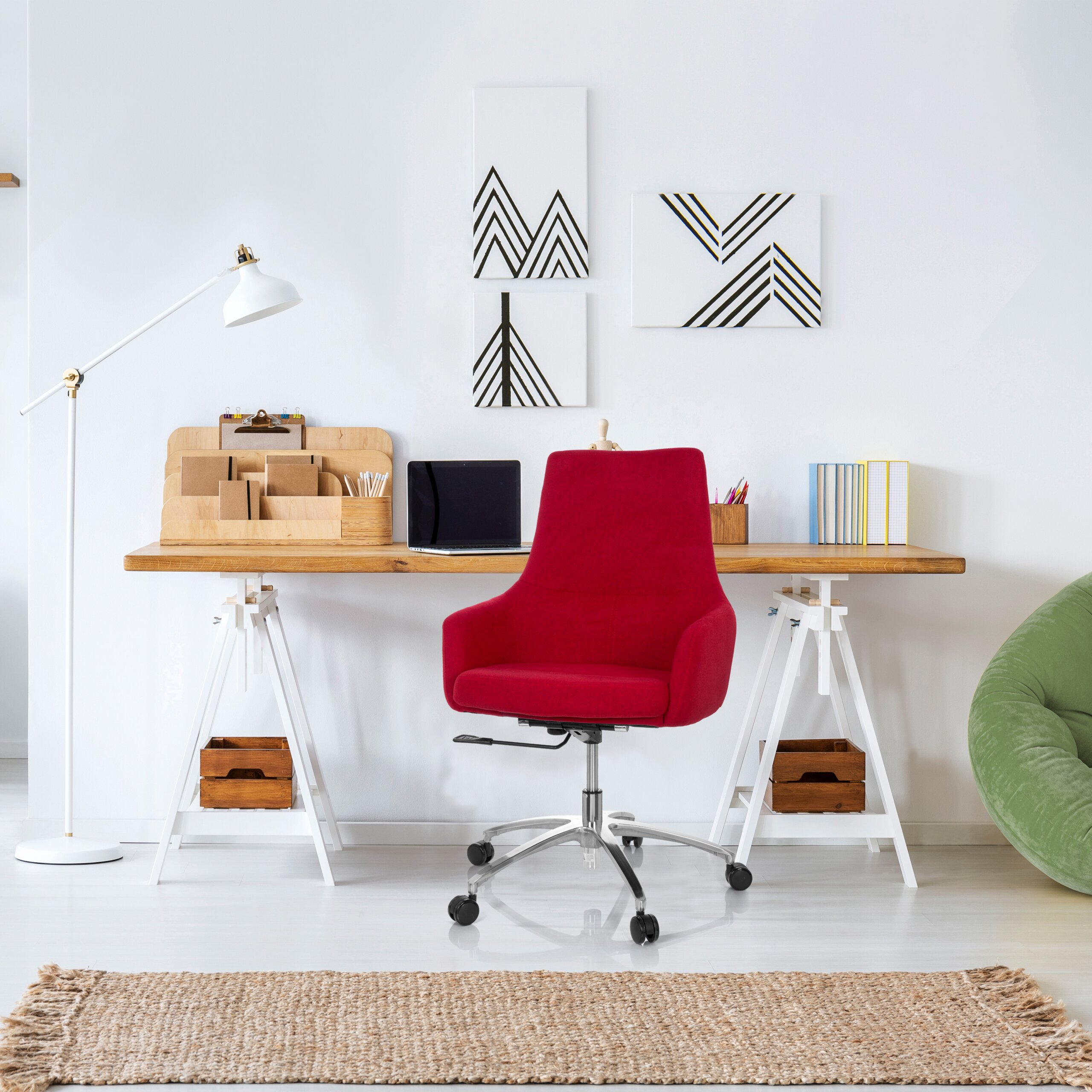 Moderner Arbeitsplatz mit rotem Stuhl, Holztisch, Laptop, Lampe und abstrakten Kunstwerken an der weißen Wand.
