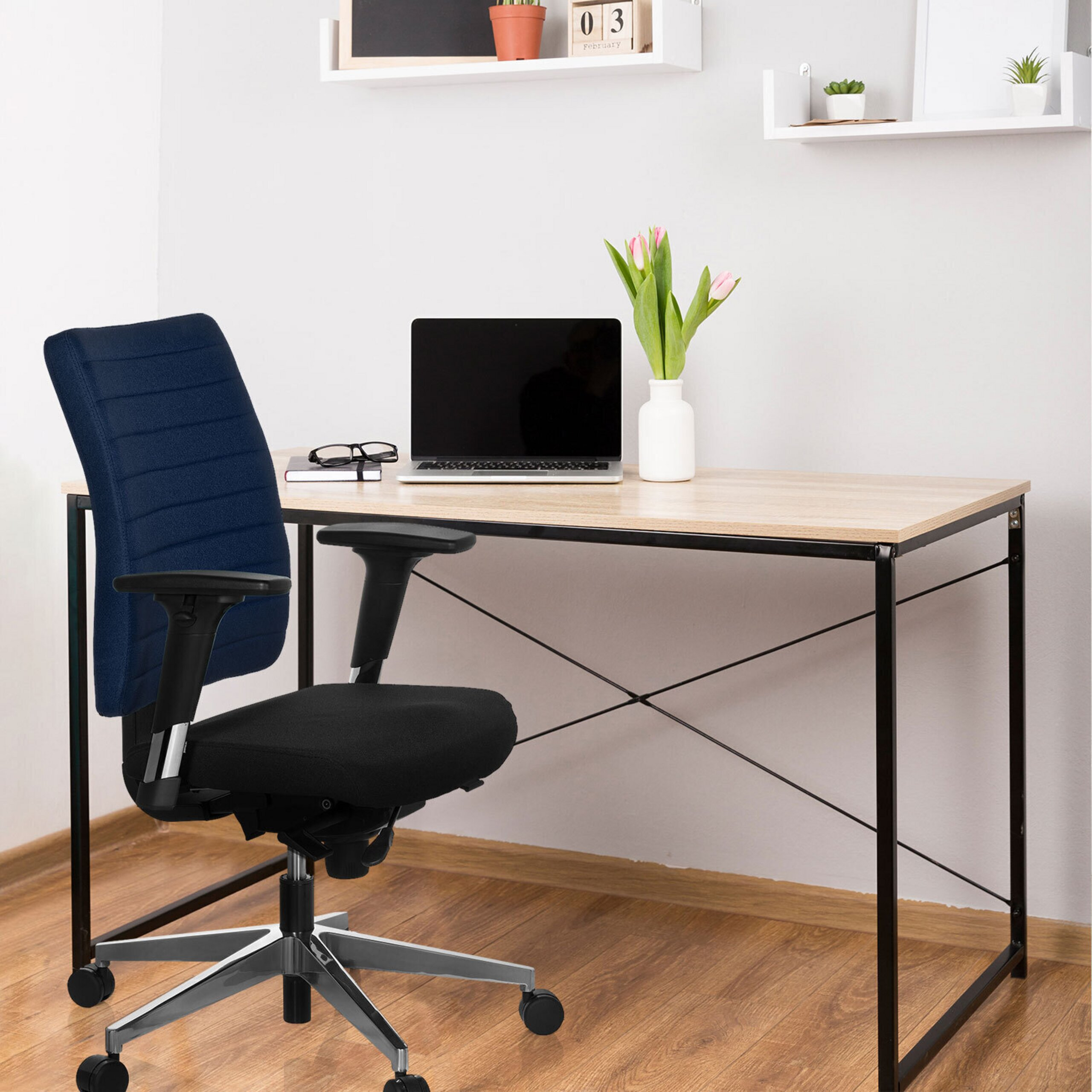 Ein moderner Schreibtisch mit Laptop, Tulpenvase und blauem Bürostuhl in einem hellen Raum.