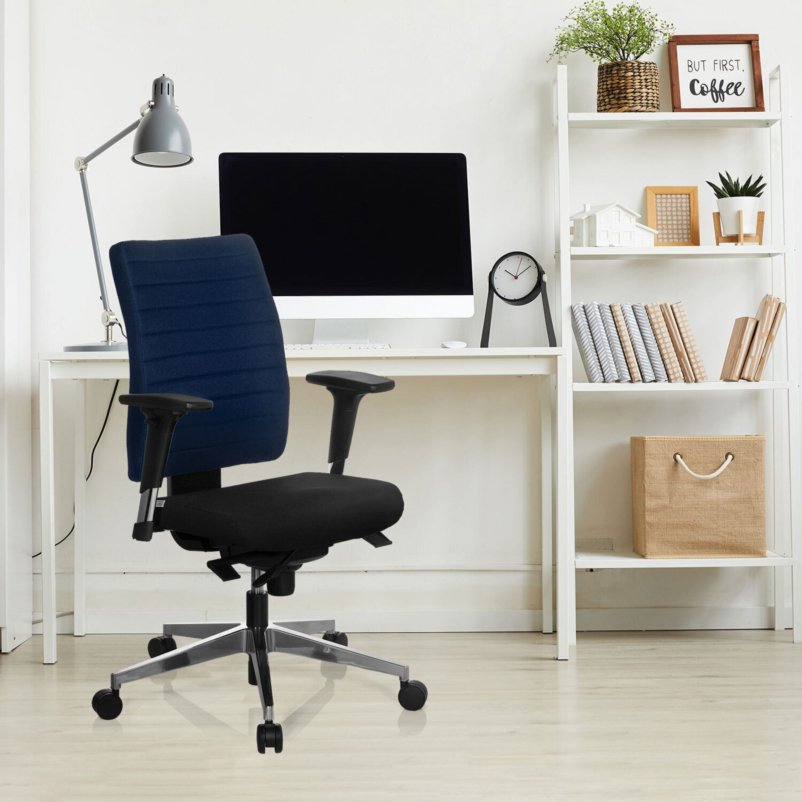 Ein blau-schwarzer Bürostuhl steht vor einem weißen Schreibtisch mit Computer und Regal.