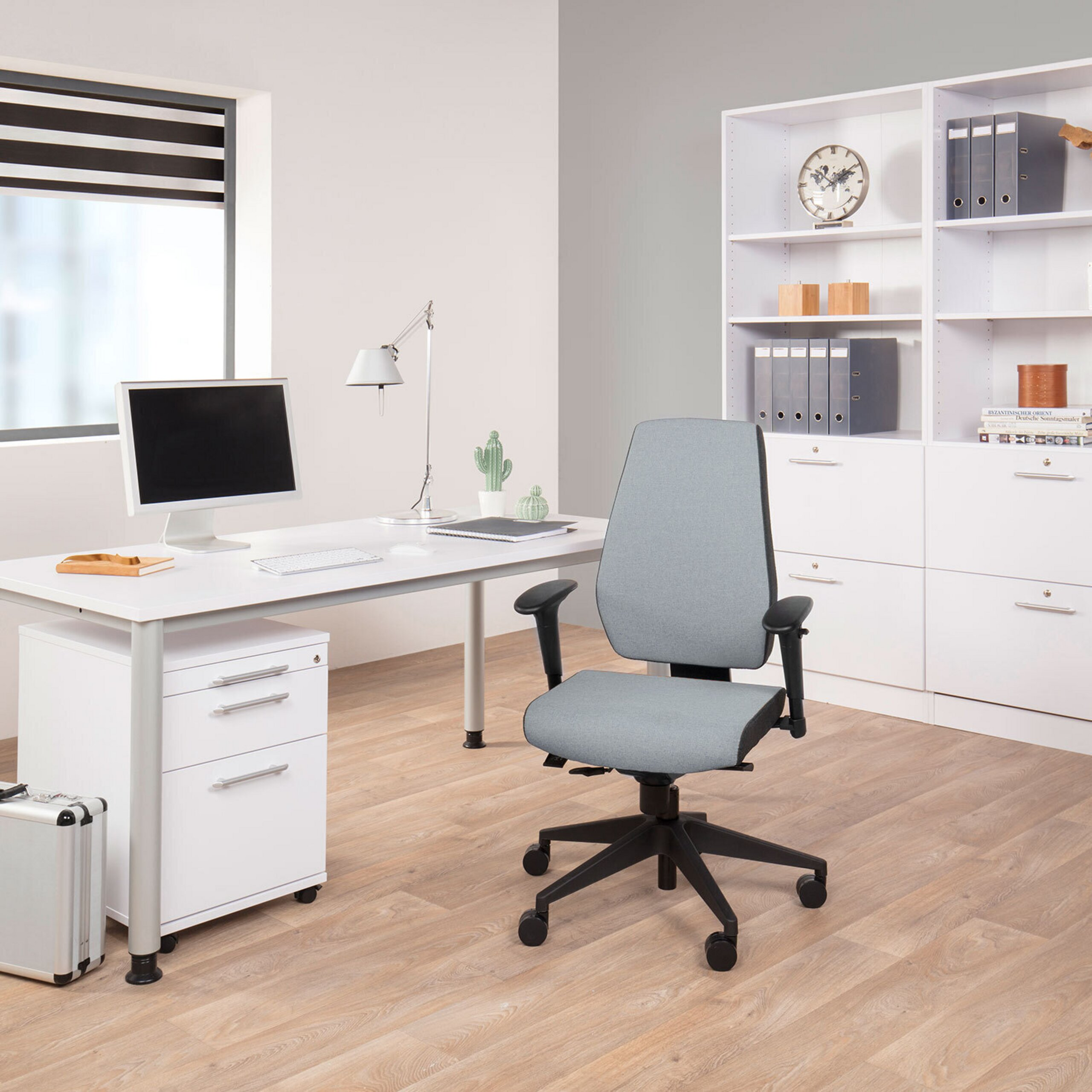 Moderne Bueroumggebung mit weißem Schreibtisch, grauen Stuhl, Computer und großem Regal auf Holzboden.