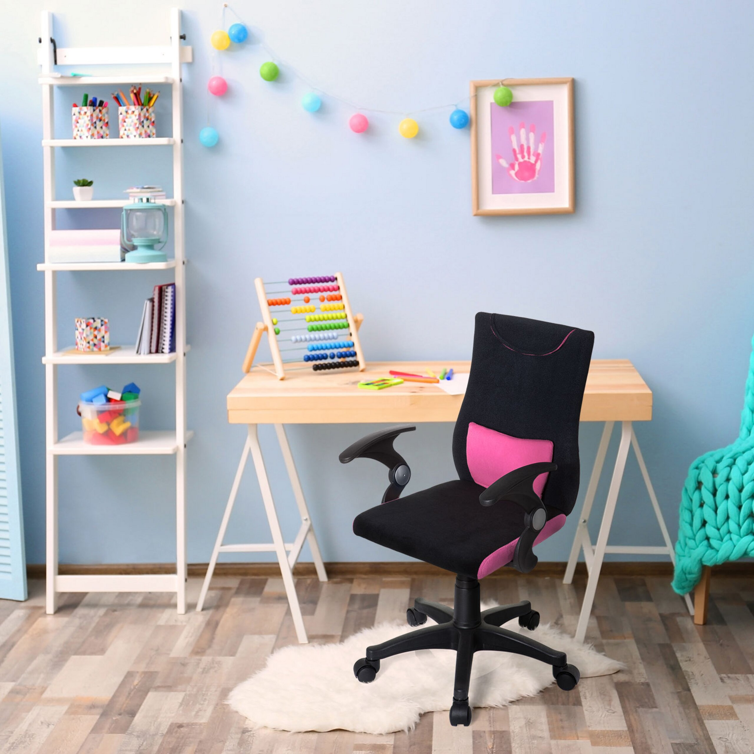 Ein schwarzer Schreibtischstuhl mit pinkem Kissen in einem hellblauen Kinderzimmer mit Holzmöbeln und Spielzeug.