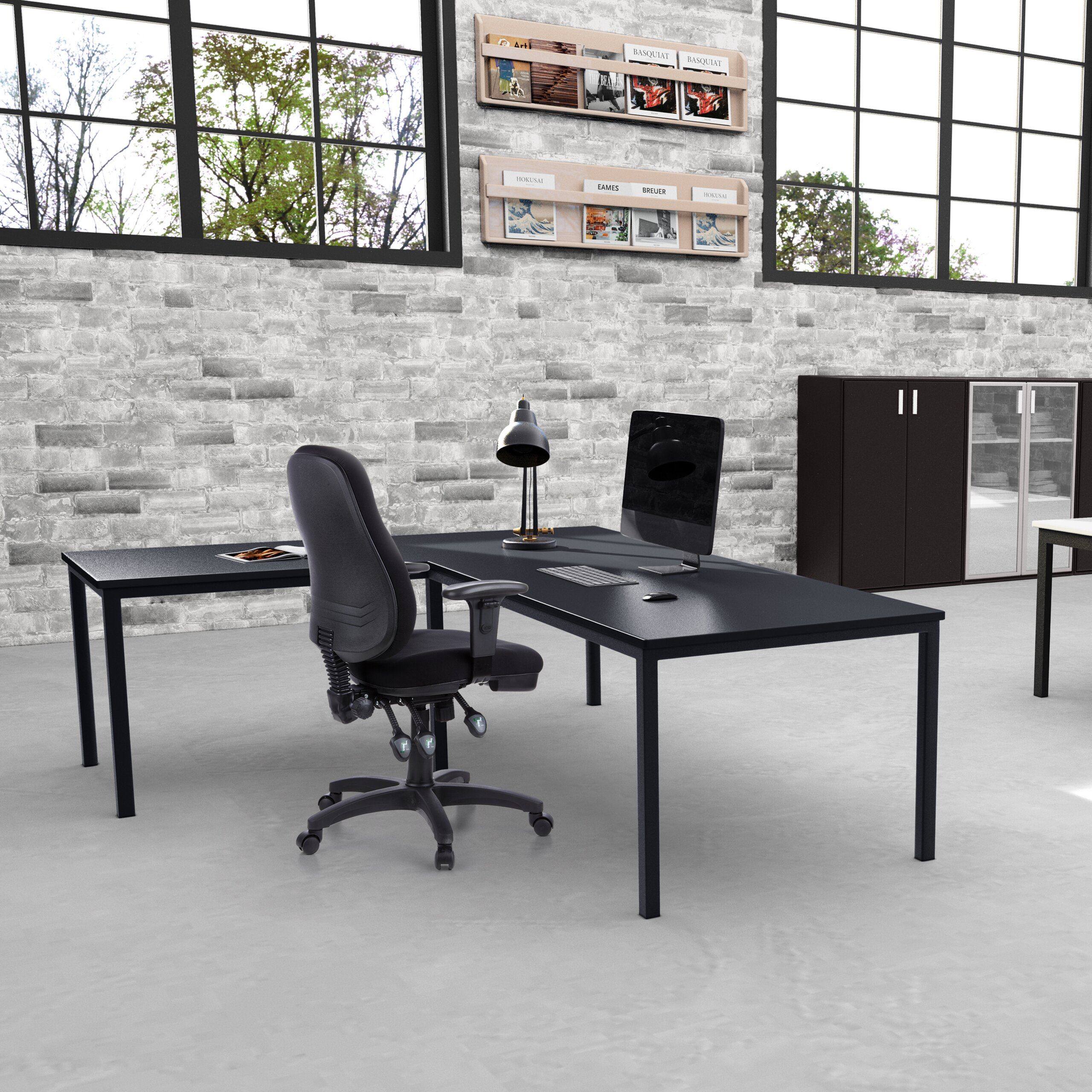 Moderne Büroarbeitsplatz mit schwarzem Schreibtisch, Drehstuhl, Computer, Lampe vor grauer Backsteinwand und Fenstern.