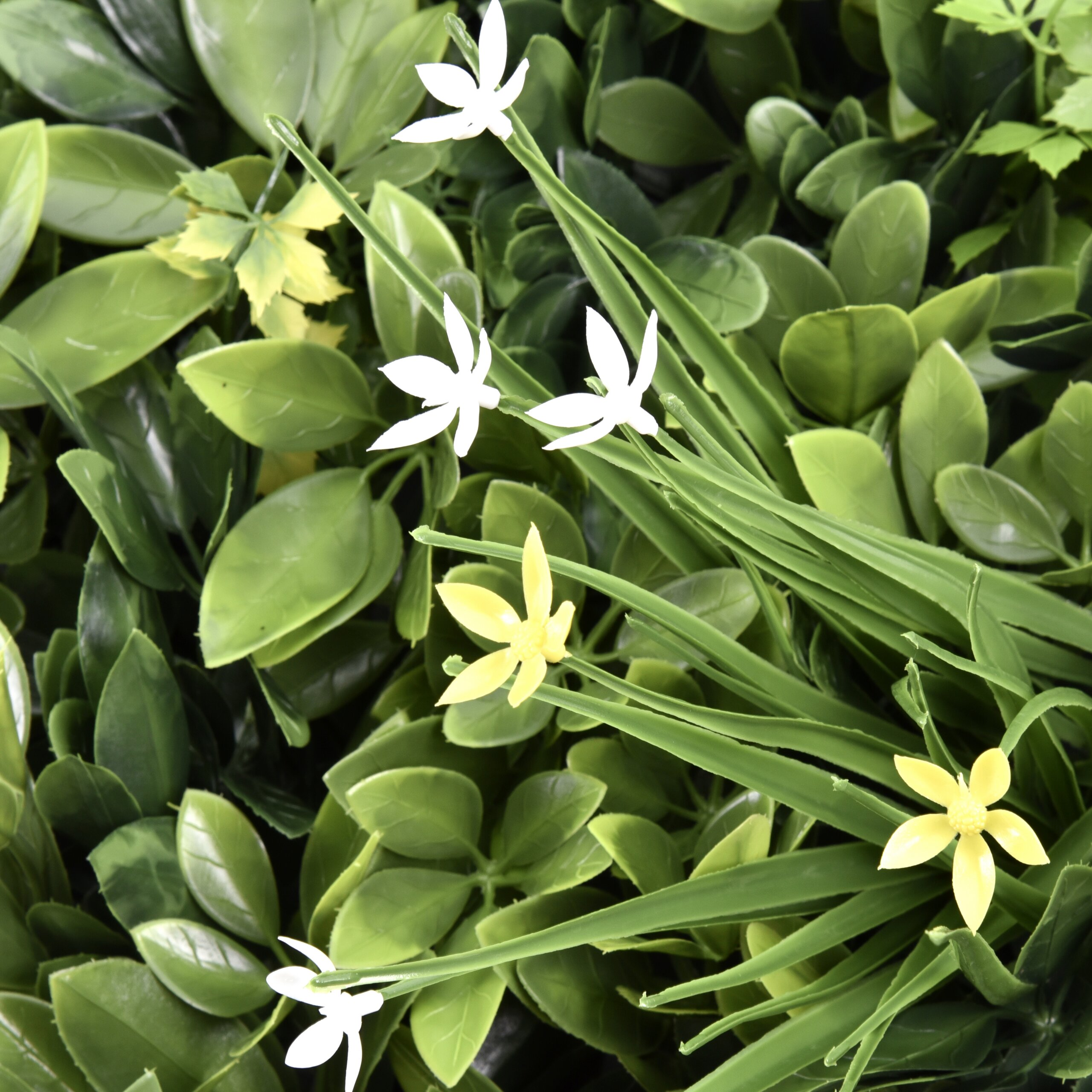 Künstliche weiße und gelbe Blumen ragen aus einem dichten Hintergrund aus grünen Blättern hervor.