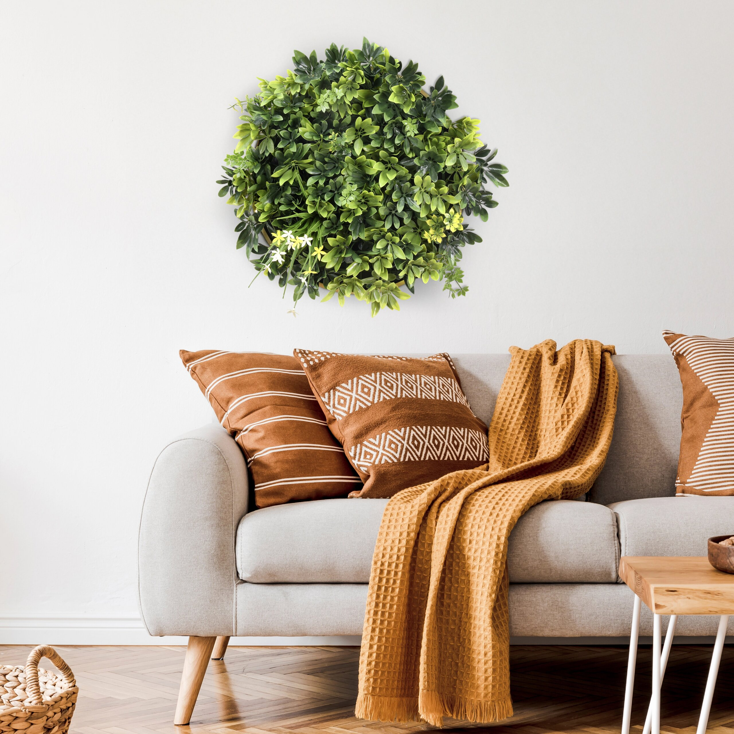 Ein graues Sofa mit braunen Kissen und einer orangefarbenen Decke steht unter runder Pflanzenwandkunst.