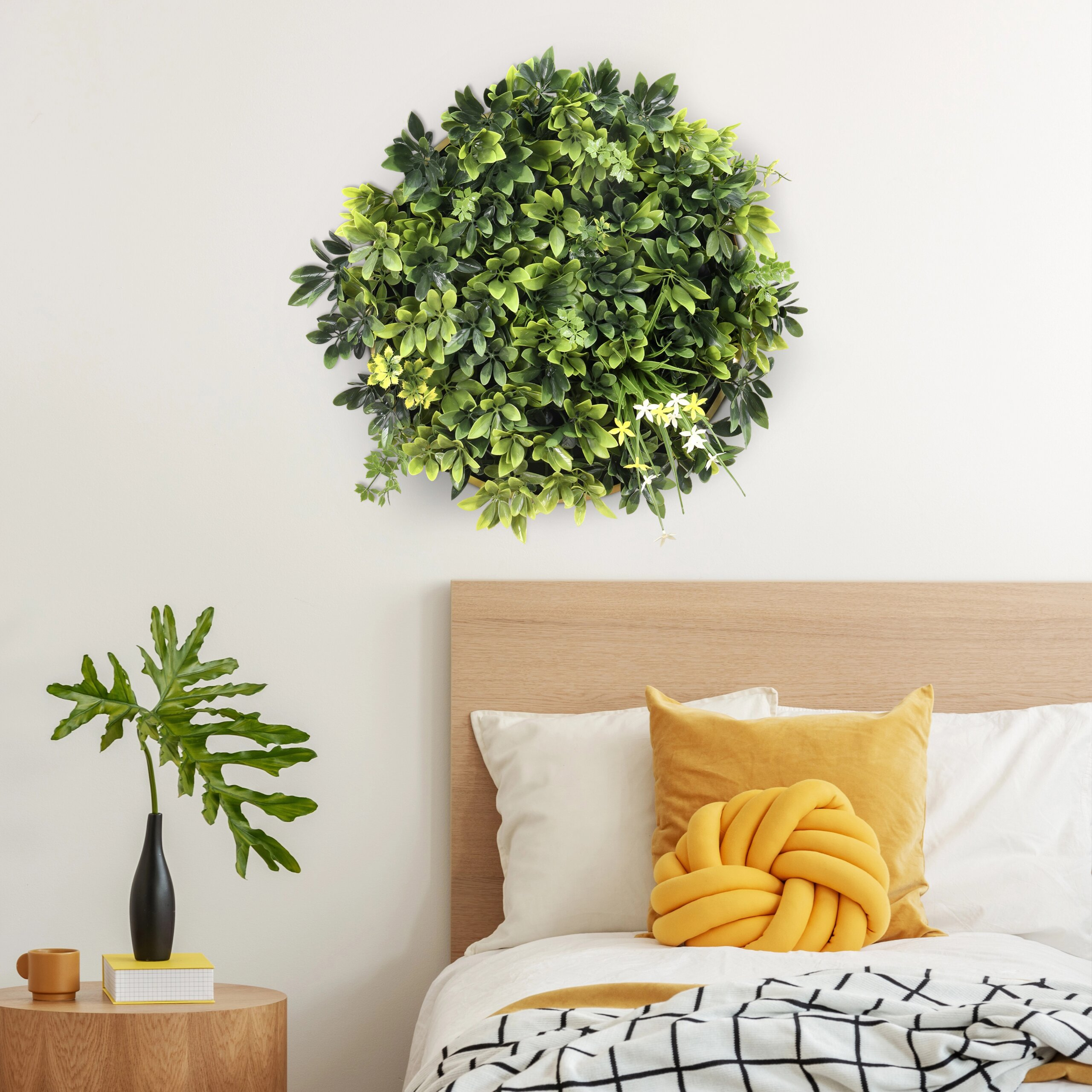 Schlafzimmer mit Holzbett, gelben Kissen, runder Grünpflanzen-Wandkunst und Nachttisch mit Pflanze.