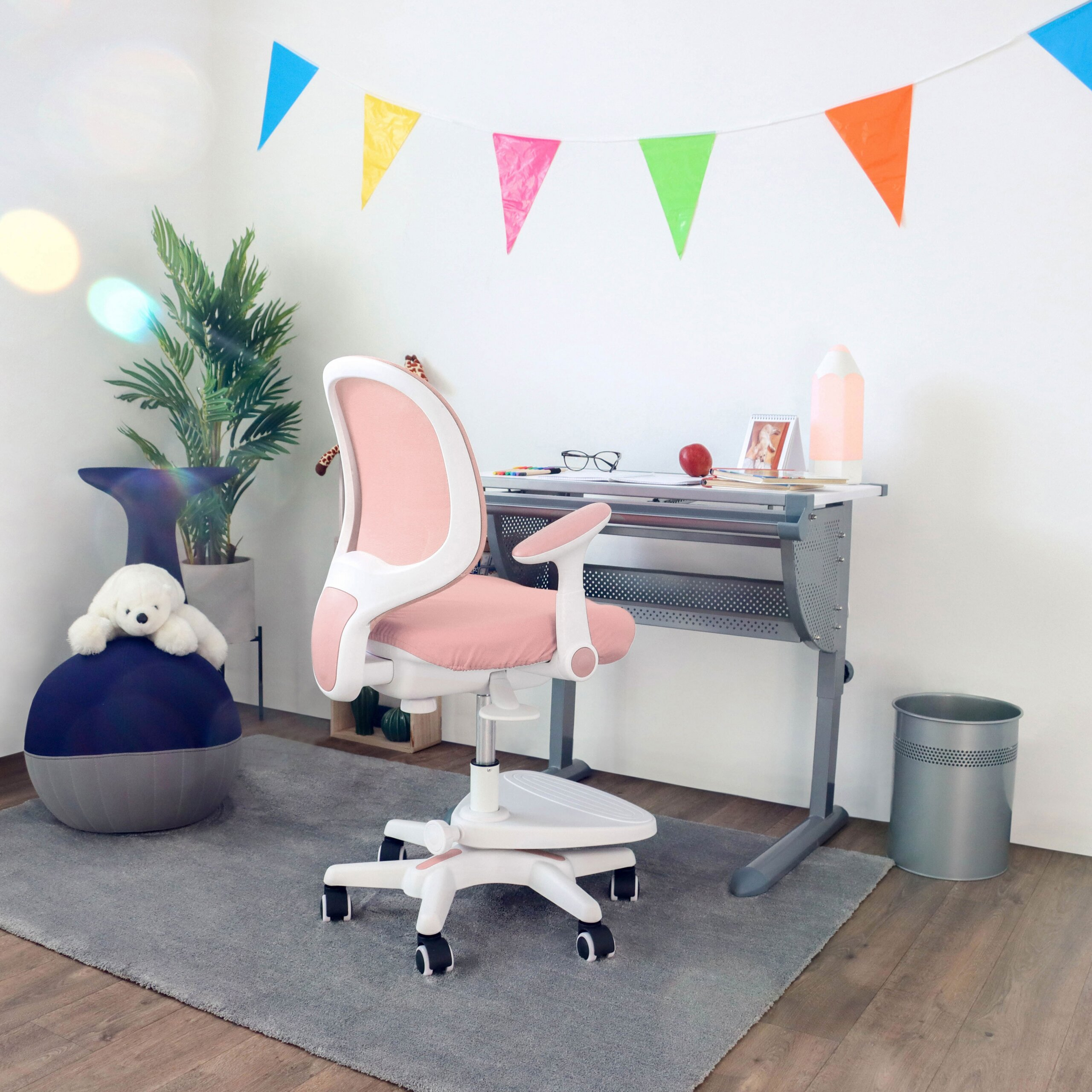 Ein Kinderzimmer mit einem rosa Stuhl, Schreibtisch, bunten Wimpeln und Deko.