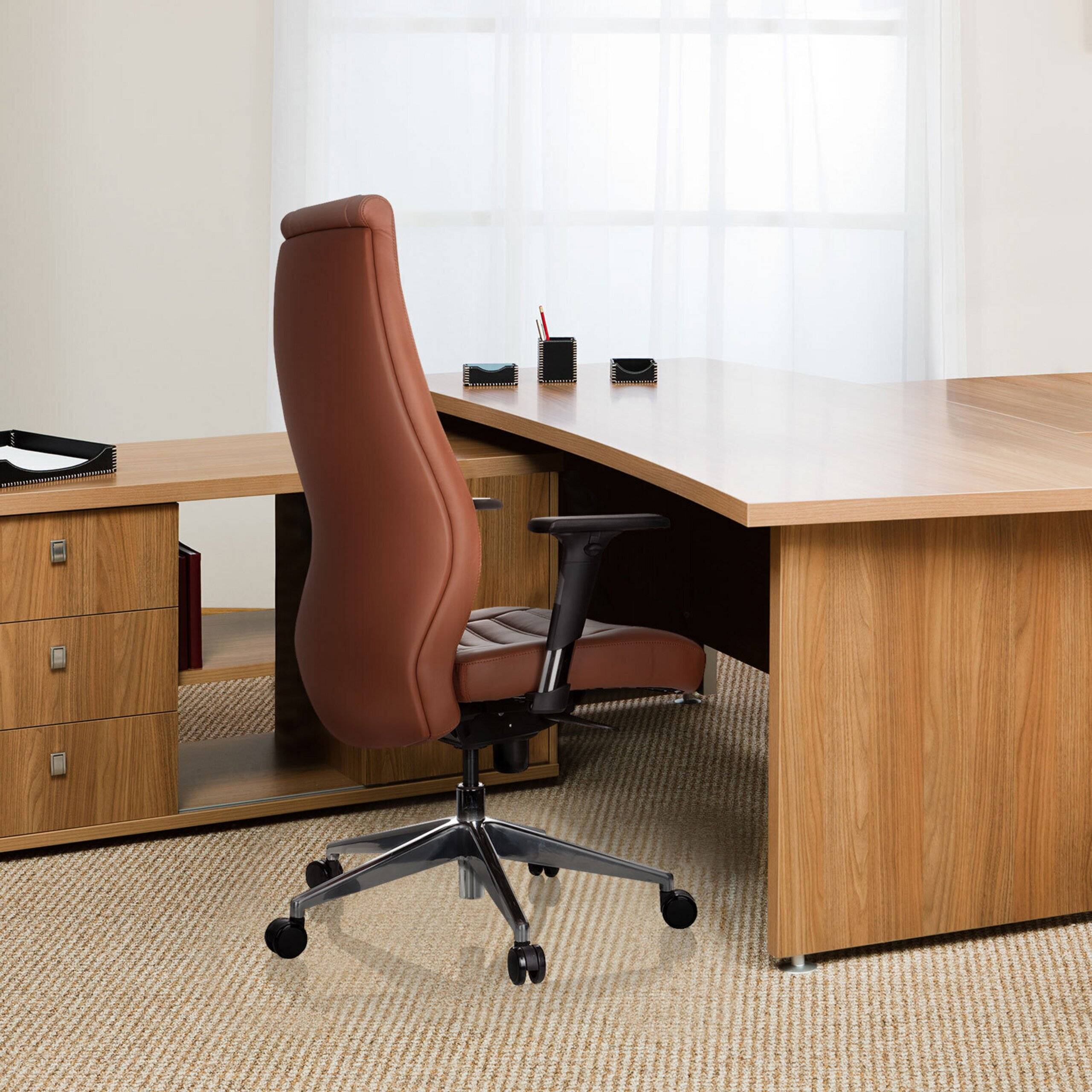 Ein brauner Leder-Bürostuhl steht vor einem Holztisch mit Schrank auf Teppichboden.