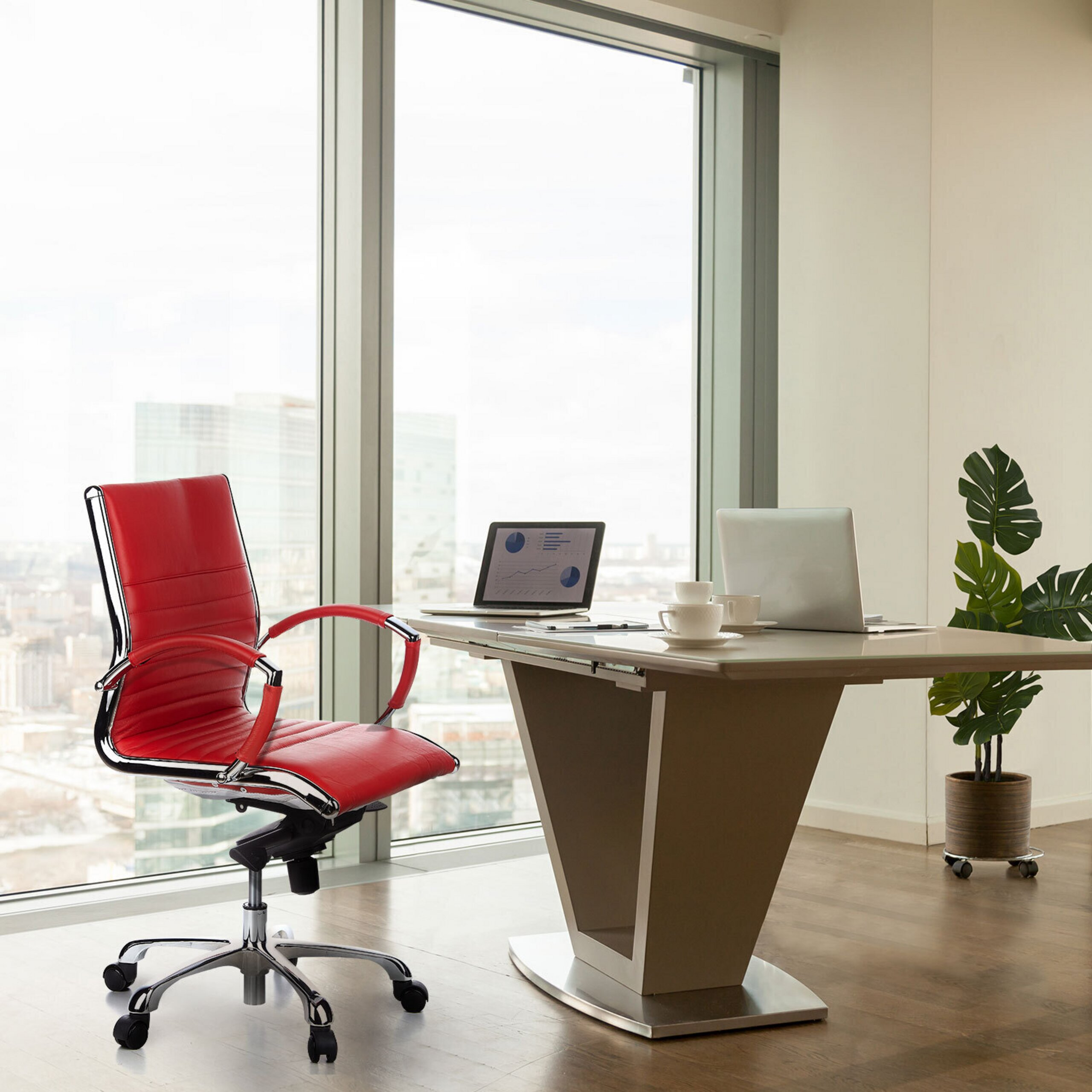 Büro mit einem roten Stuhl, Schreibtisch, zwei Laptops, Kaffeetassen und einer Topfpflanze vor großem Fenster.