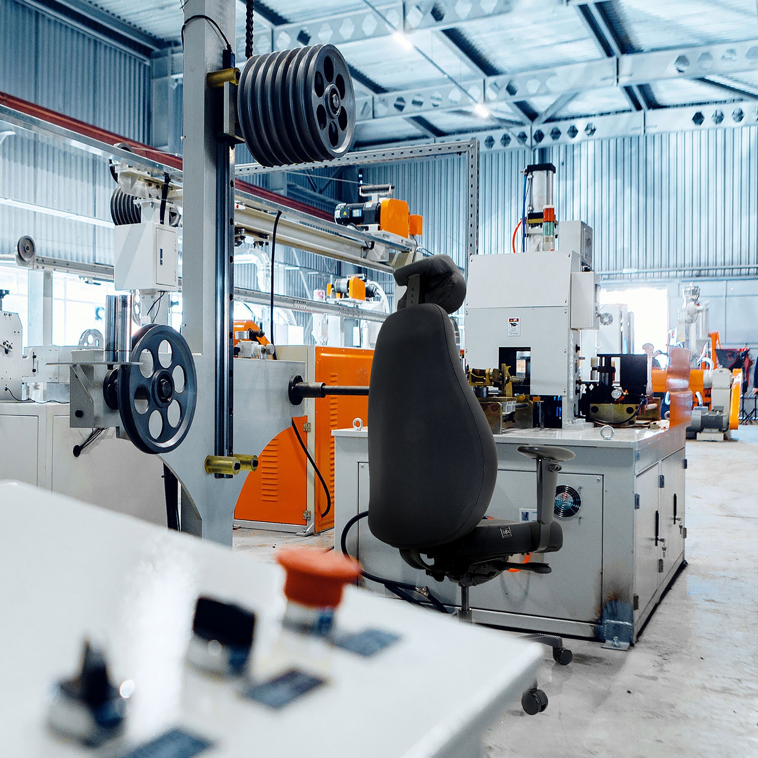 Industrielle Fabrikhalle mit Maschinen und einem ergonomischen schwarzen Stuhl im Vordergrund.