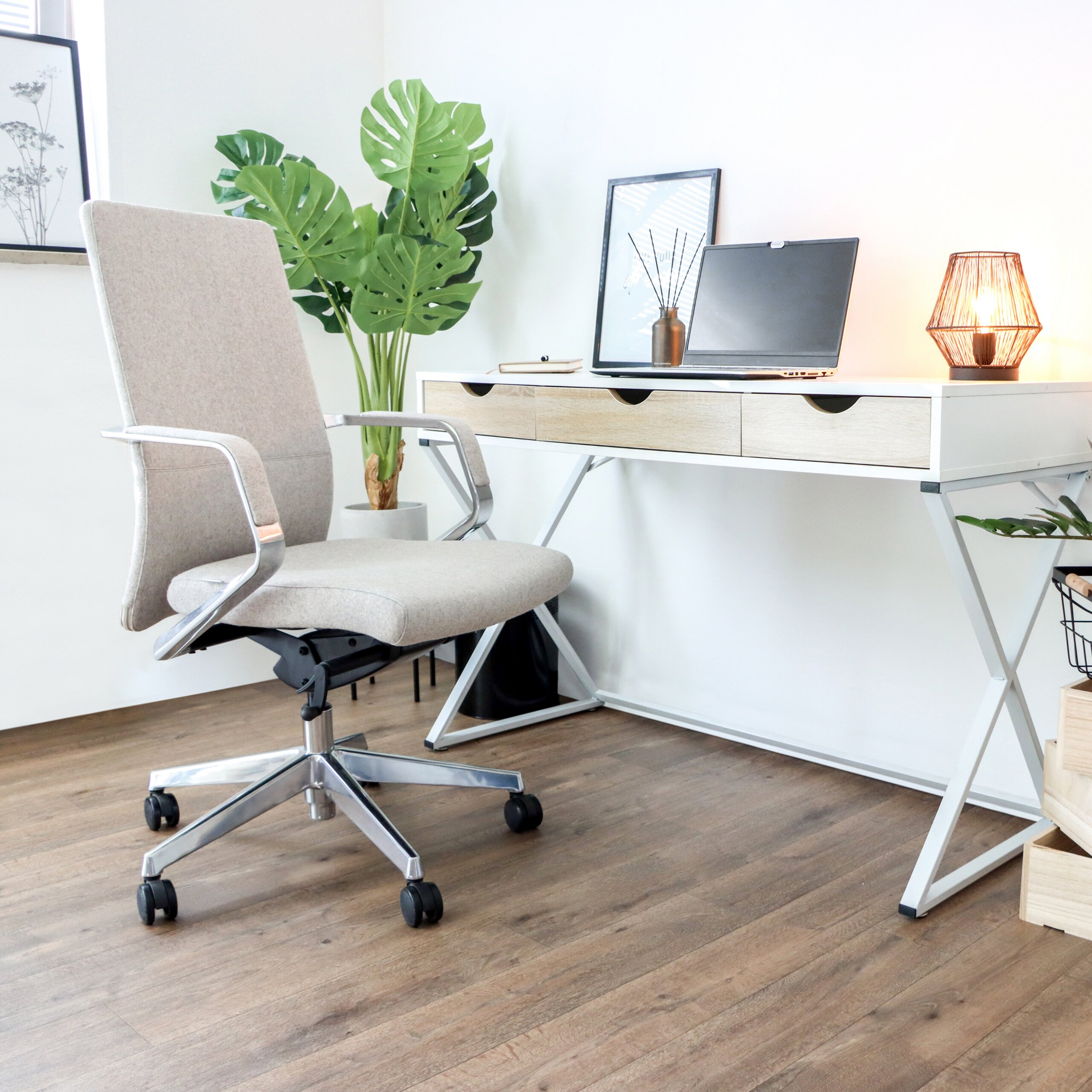 Helles Büro mit beige Bürostuhl, weißem Holztisch mit Laptop, Lampe und großer Monstera im Hintergrund.