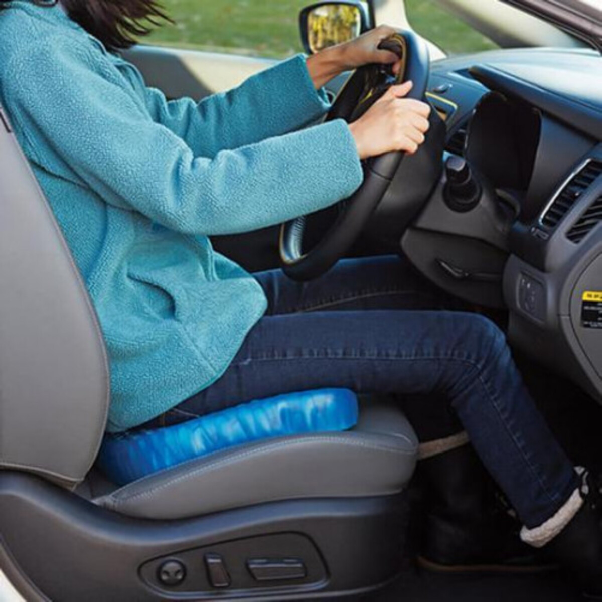 Una mujer conduciendo un auto, sentada sobre un cojín de gel azul en el asiento del conductor.