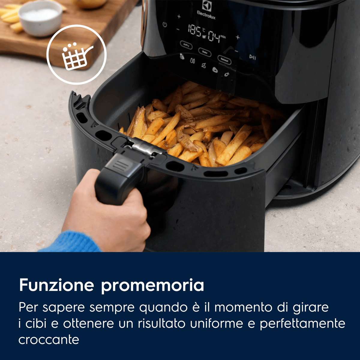 Una mano estrae il cestello di una friggitrice ad aria nera, pieno di patatine dorate.
