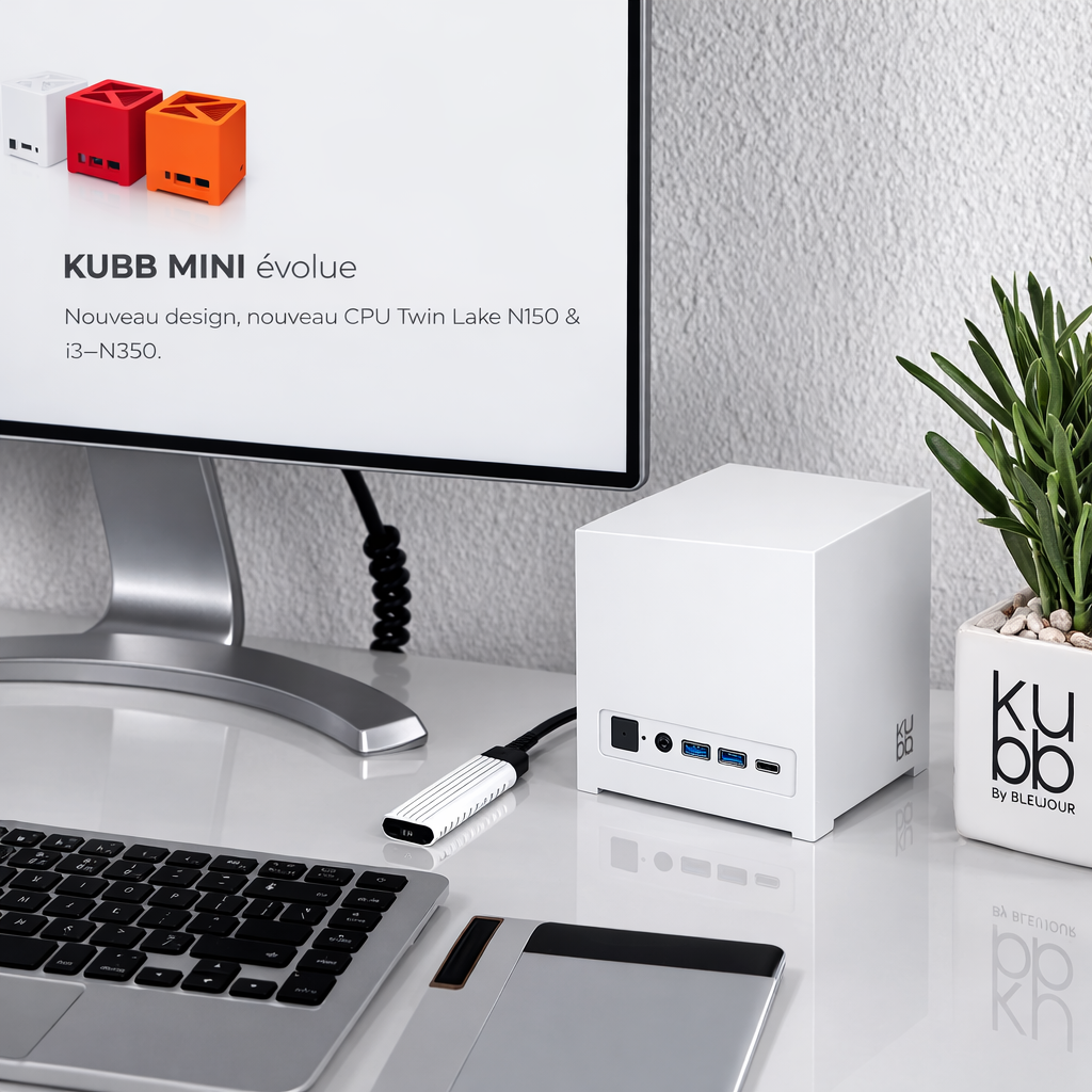 Biały mini komputer na biurku obok monitora, klawiatury, tabletu graficznego i rośliny w doniczce.
