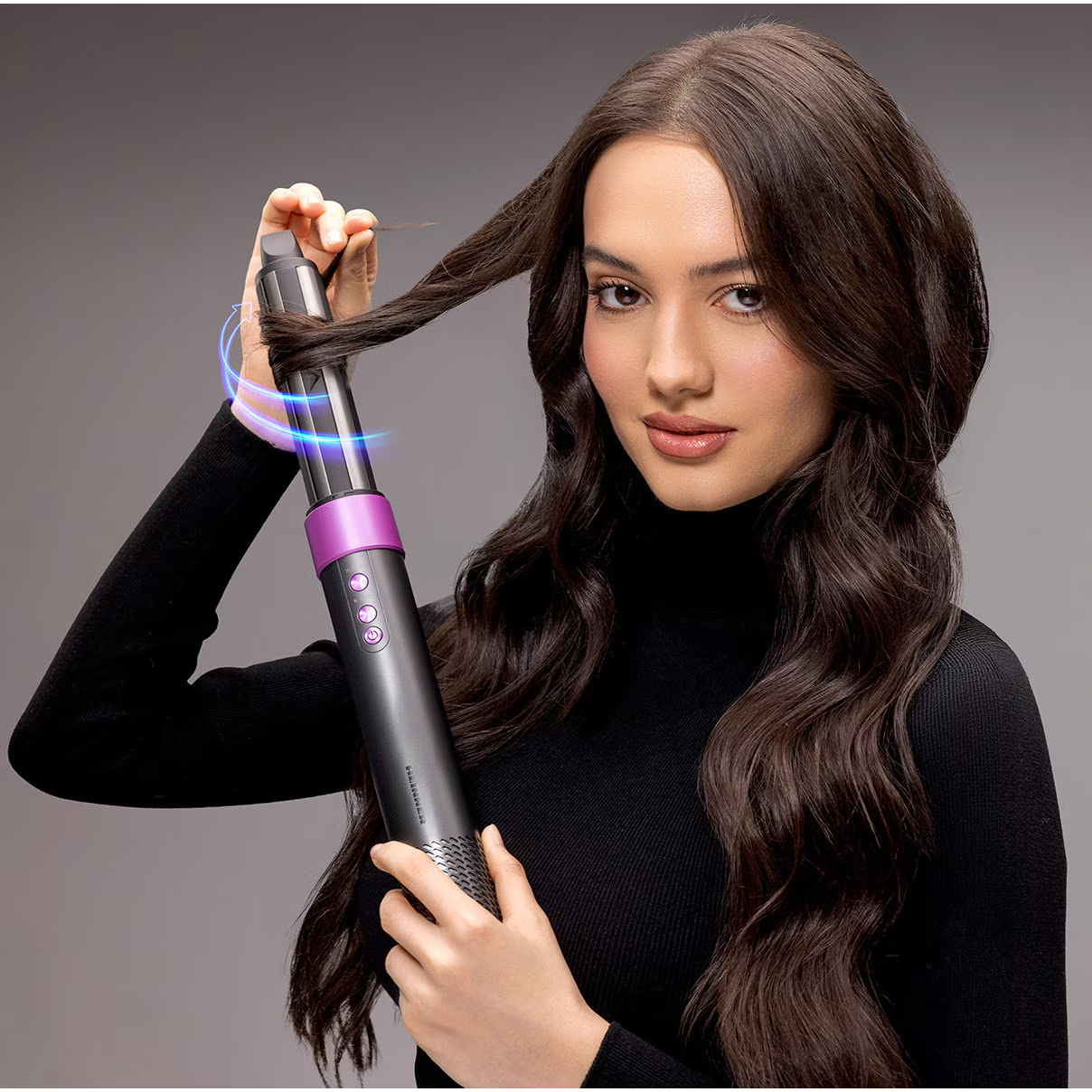 Une femme en haut noir utilise un boucleur automatique gris et violet sur ses cheveux.