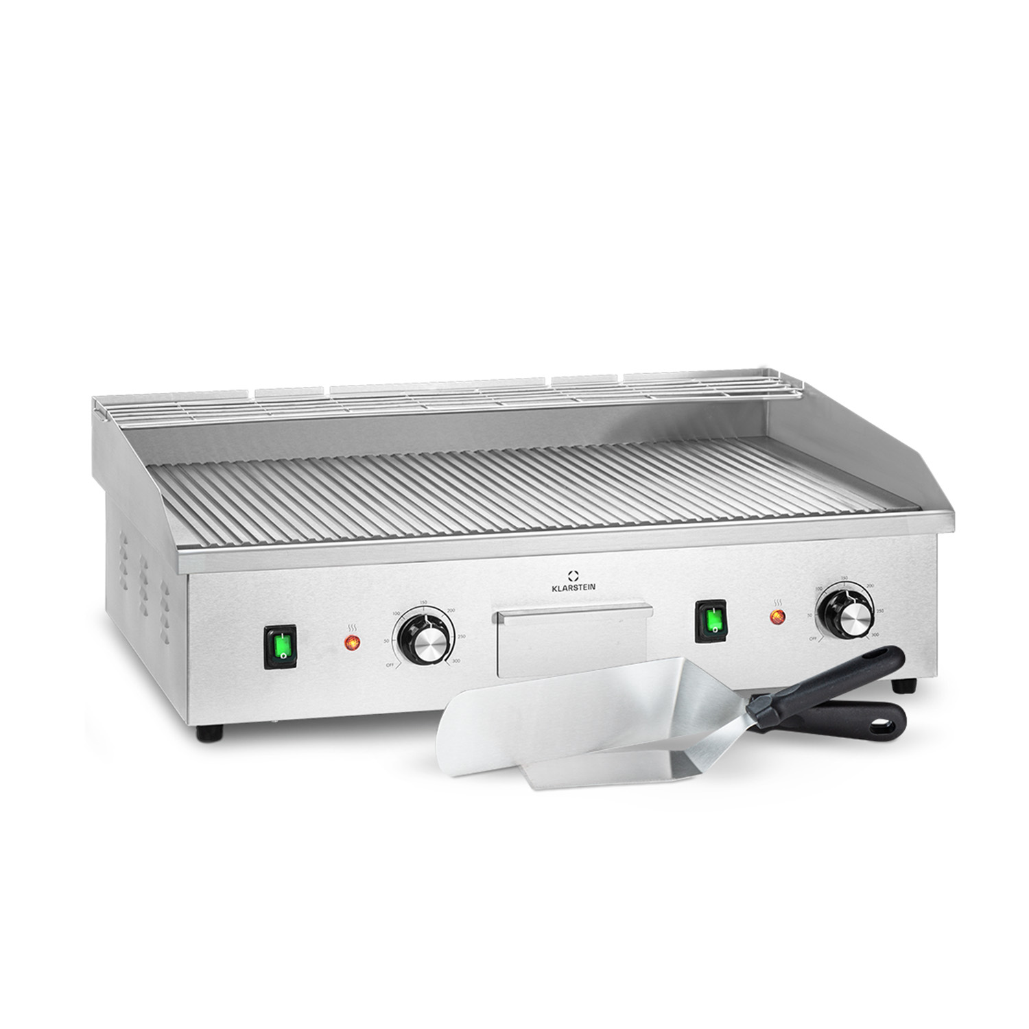 Una griglia elettrica argentata con superficie scanalata, controlli di temperatura e due spatole su sfondo bianco.