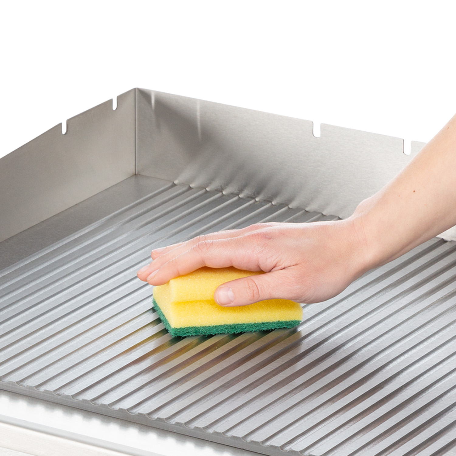 Una mano pulisce con una spugna gialla e verde una superficie in acciaio inox.