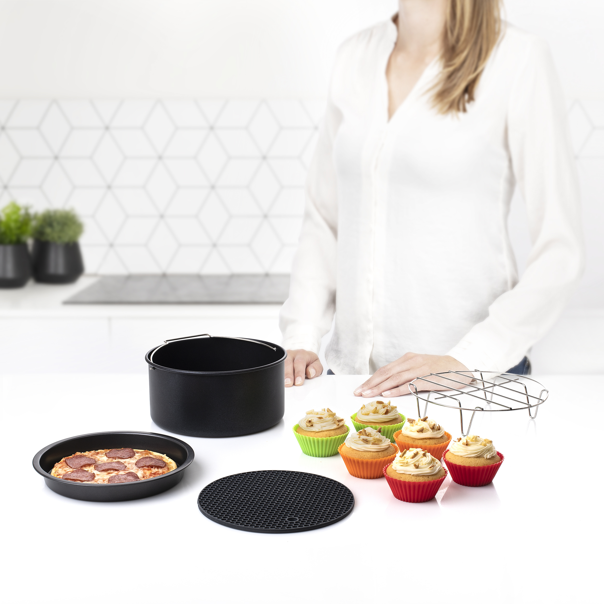 Una donna dietro un bancone bianco mostra accessori da forno, tra cui cupcake, una teglia per pizza e una pentola.