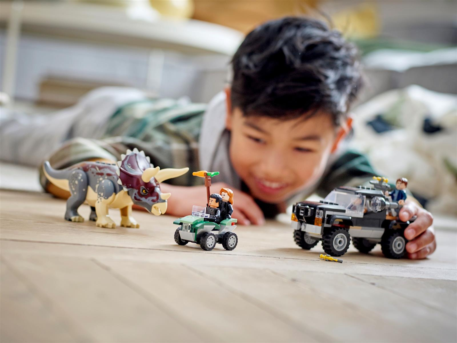 Ein Junge spielt auf dem Holzboden mit Lego-Dinosauriern und Autos.