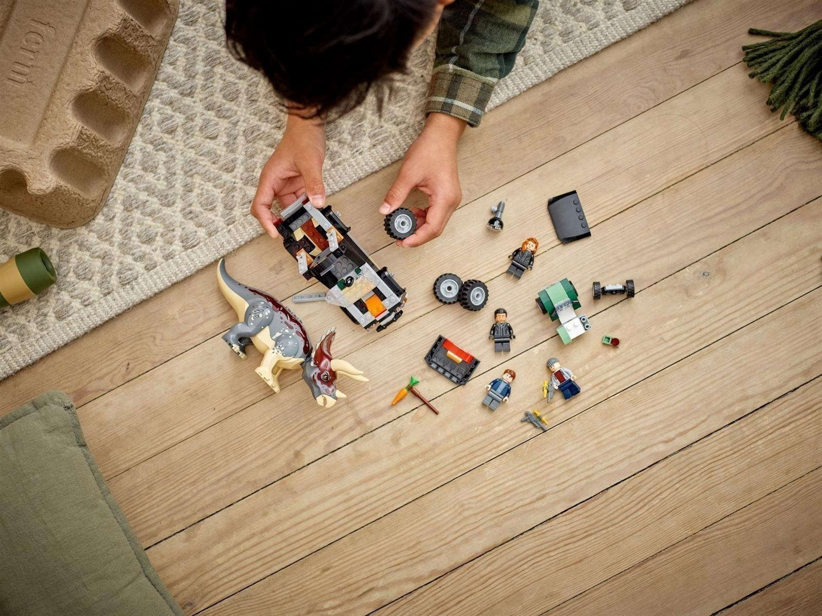 Ein Kind baut ein Lego-Auto auf einem Holzboden mit Figuren und einem Dinosaurier.