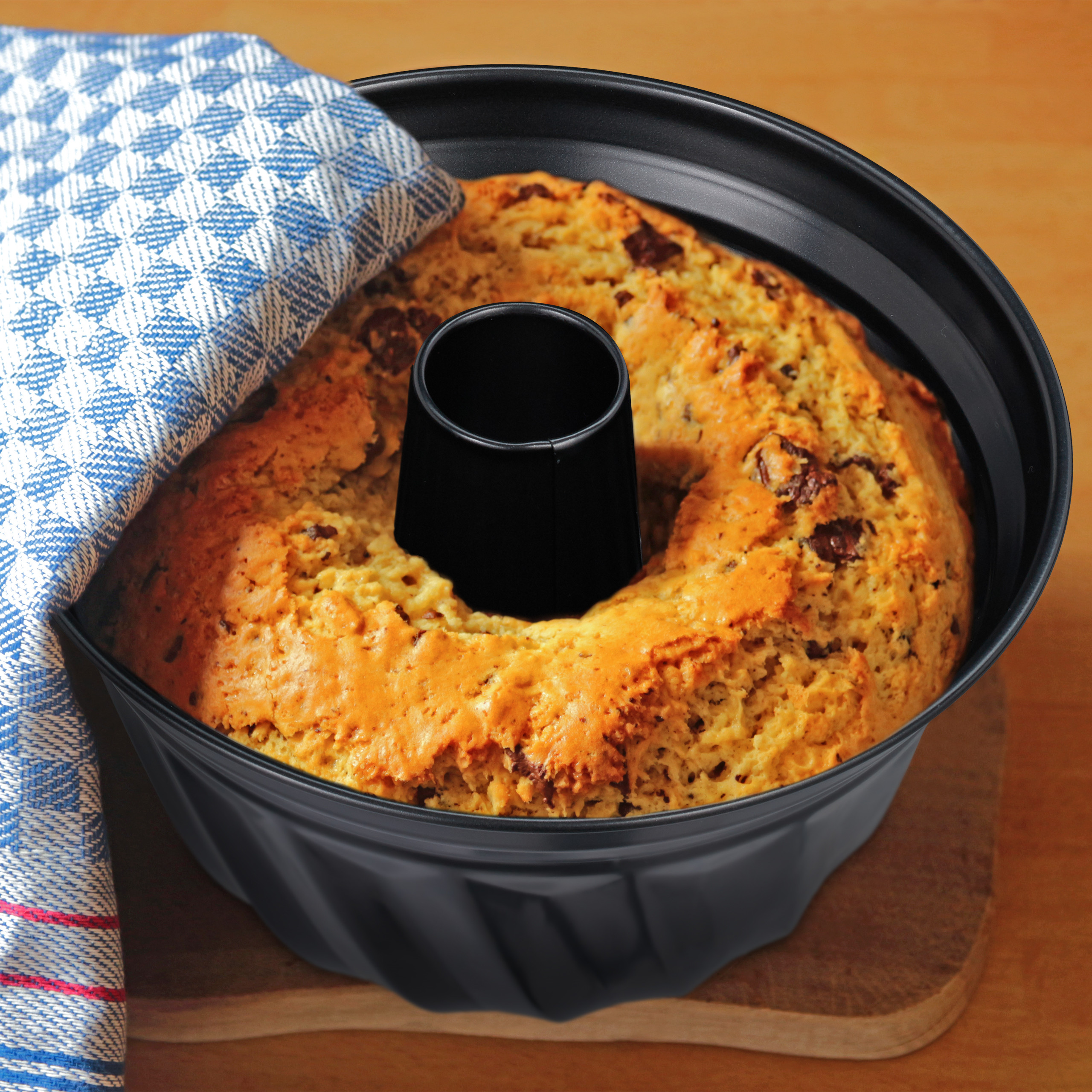 Ein gebackener Kuchen mit Schokostücken in einer schwarzen Gugelhupfform mit blauem Tuch.