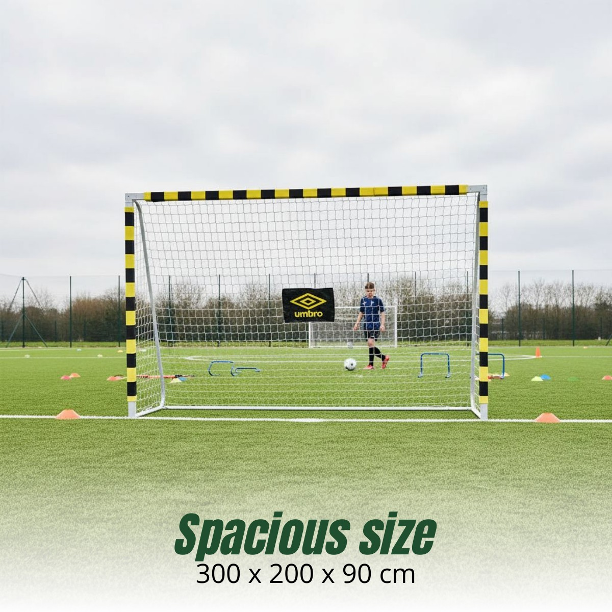 Ein Junge steht auf einem Kunstrasenfeld hinter einem gelb-schwarz umrandeten Fußballtor und hält einen Ball.