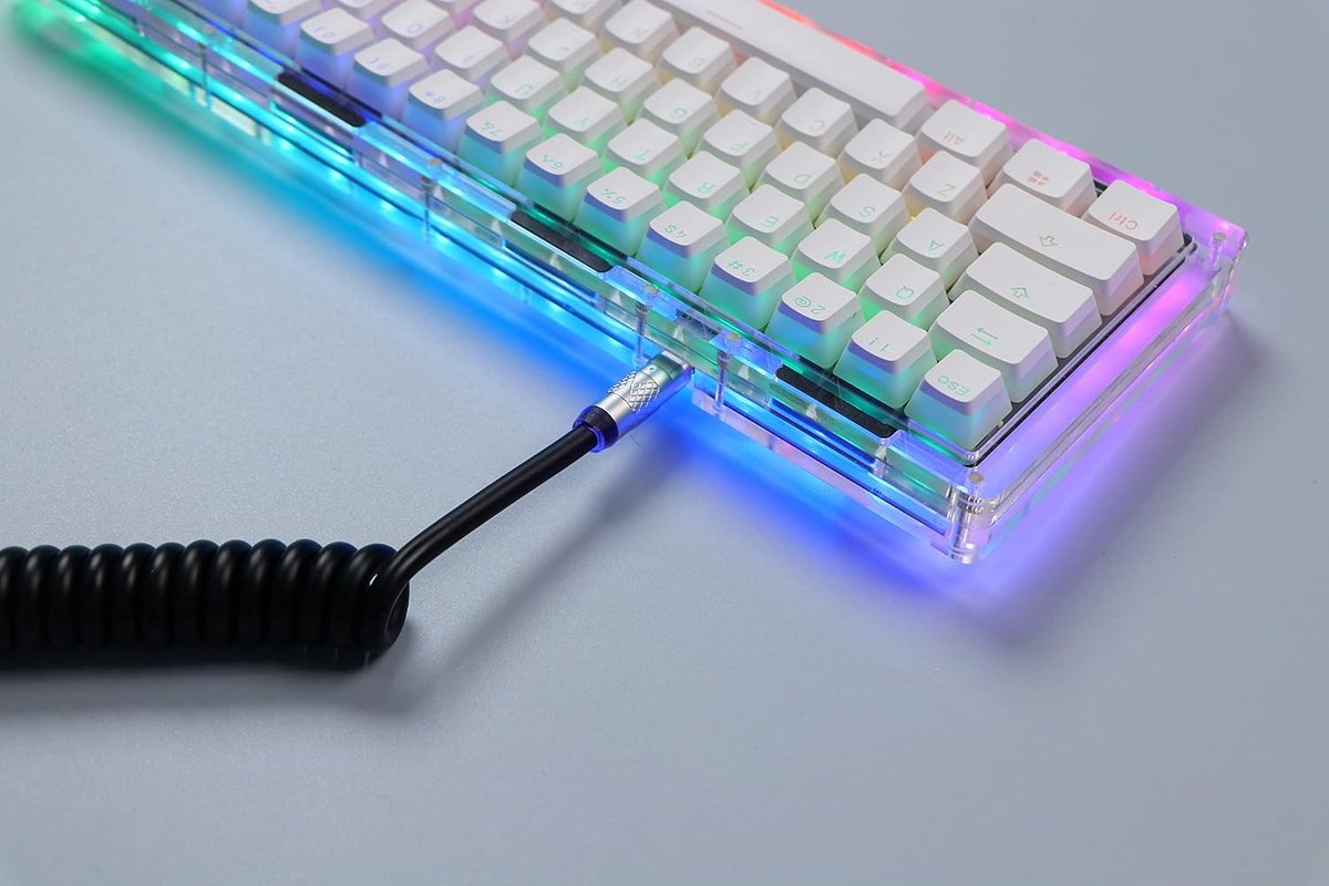 Een mechanisch toetsenbord met RGB-verlichting in een doorzichtige behuizing en aangesloten zwarte kabel op een grijs oppervlak.