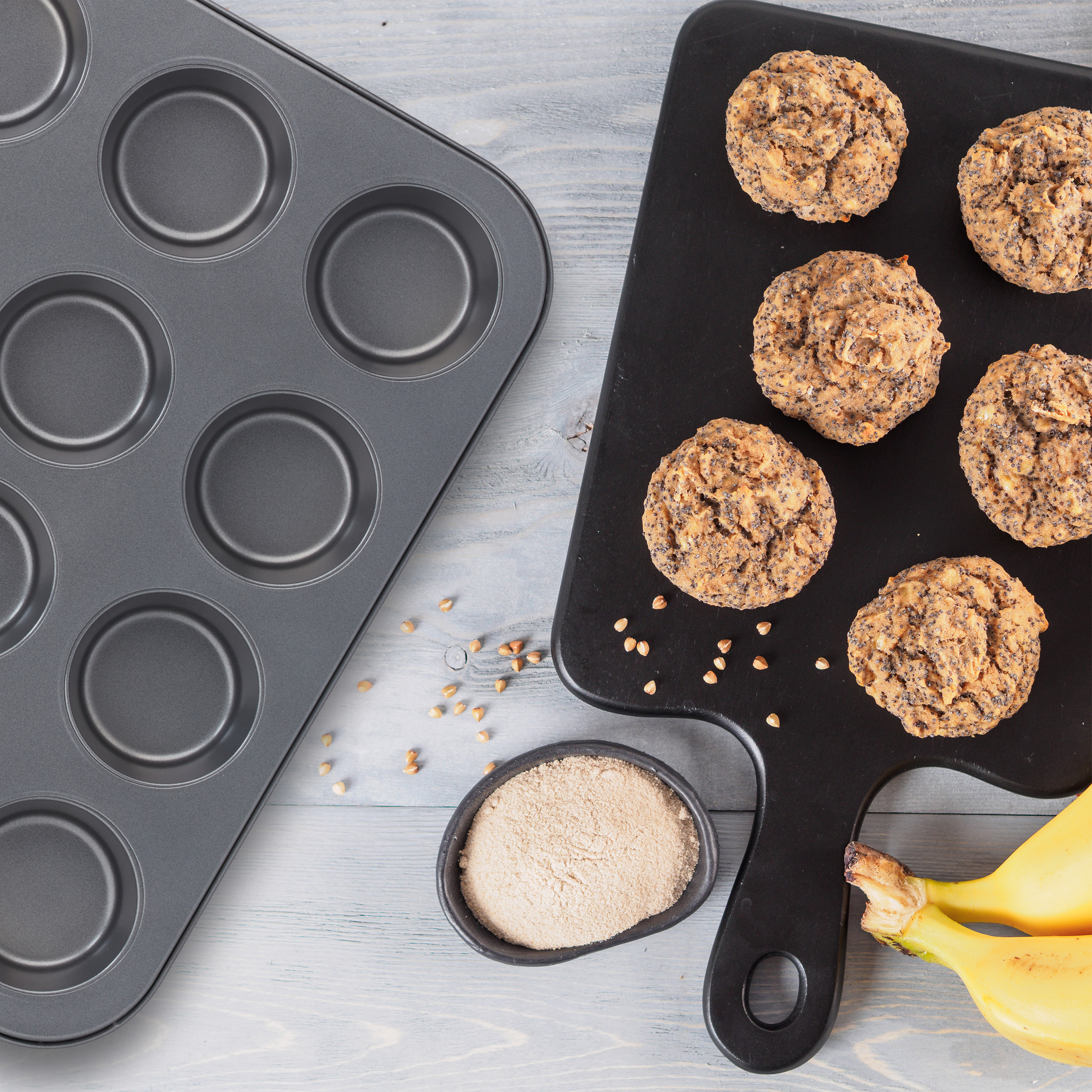 Muffins auf schwarzem Brett, leere Form, Mehl in Schüssel und Bananen auf Holz.