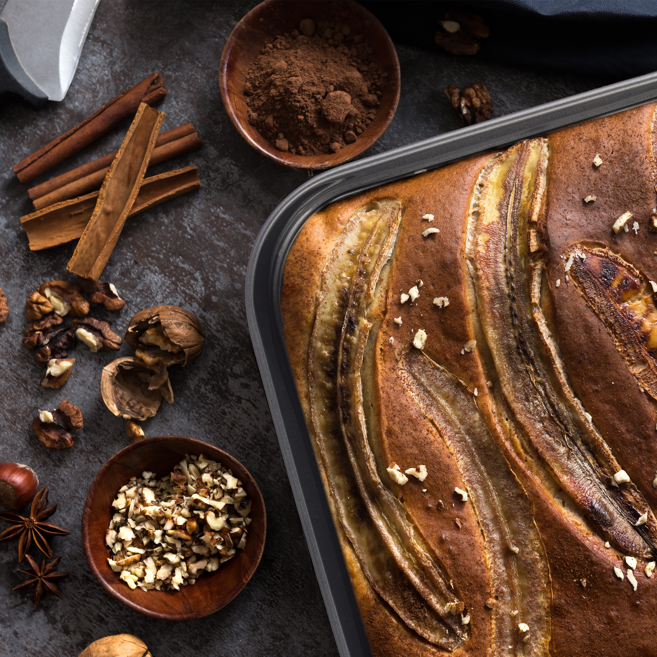 Frisch gebackener Bananenkuchen in einer Form mit Zimt, Walnüssen, Sternanis und Kakaopulver auf dunklem Tisch.