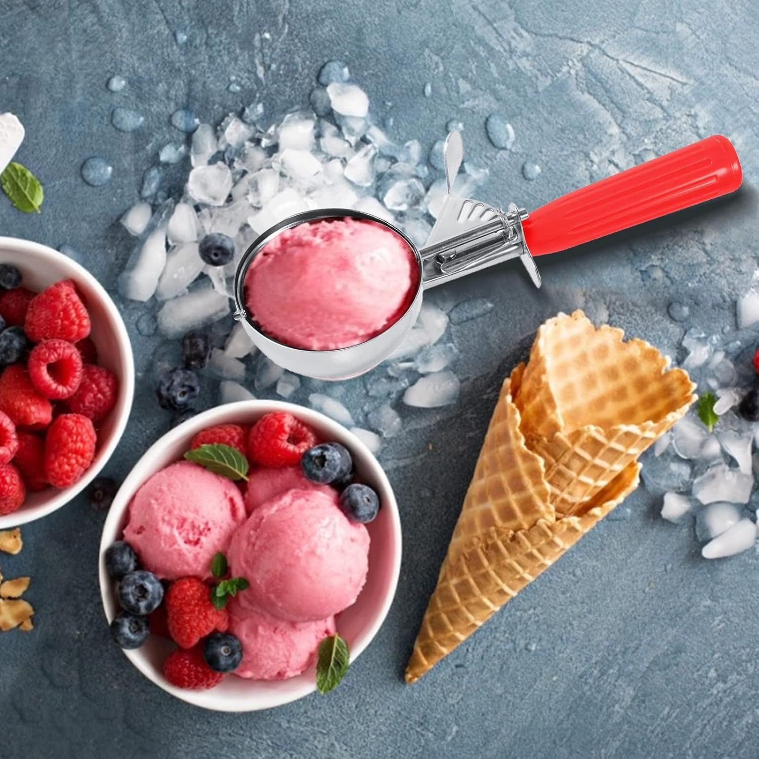 Ein rot-griffiger Eisportionierer mit rosa Kugel, Beeren und Waffeln auf grauem Hintergrund.