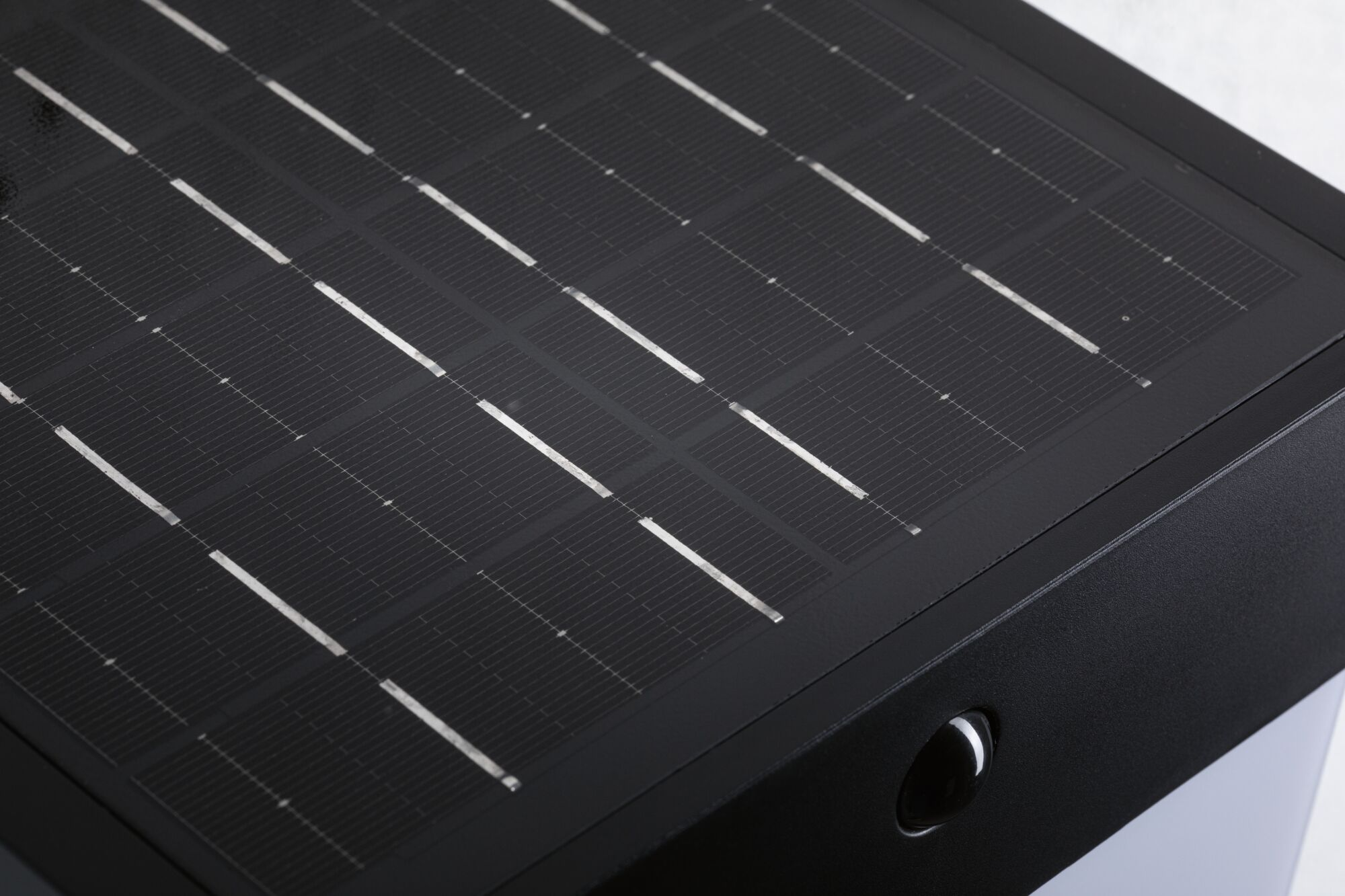 Nahaufnahme eines kleinen schwarzen Solarpanels mit silbernen Gittern und einem runden Sensor.