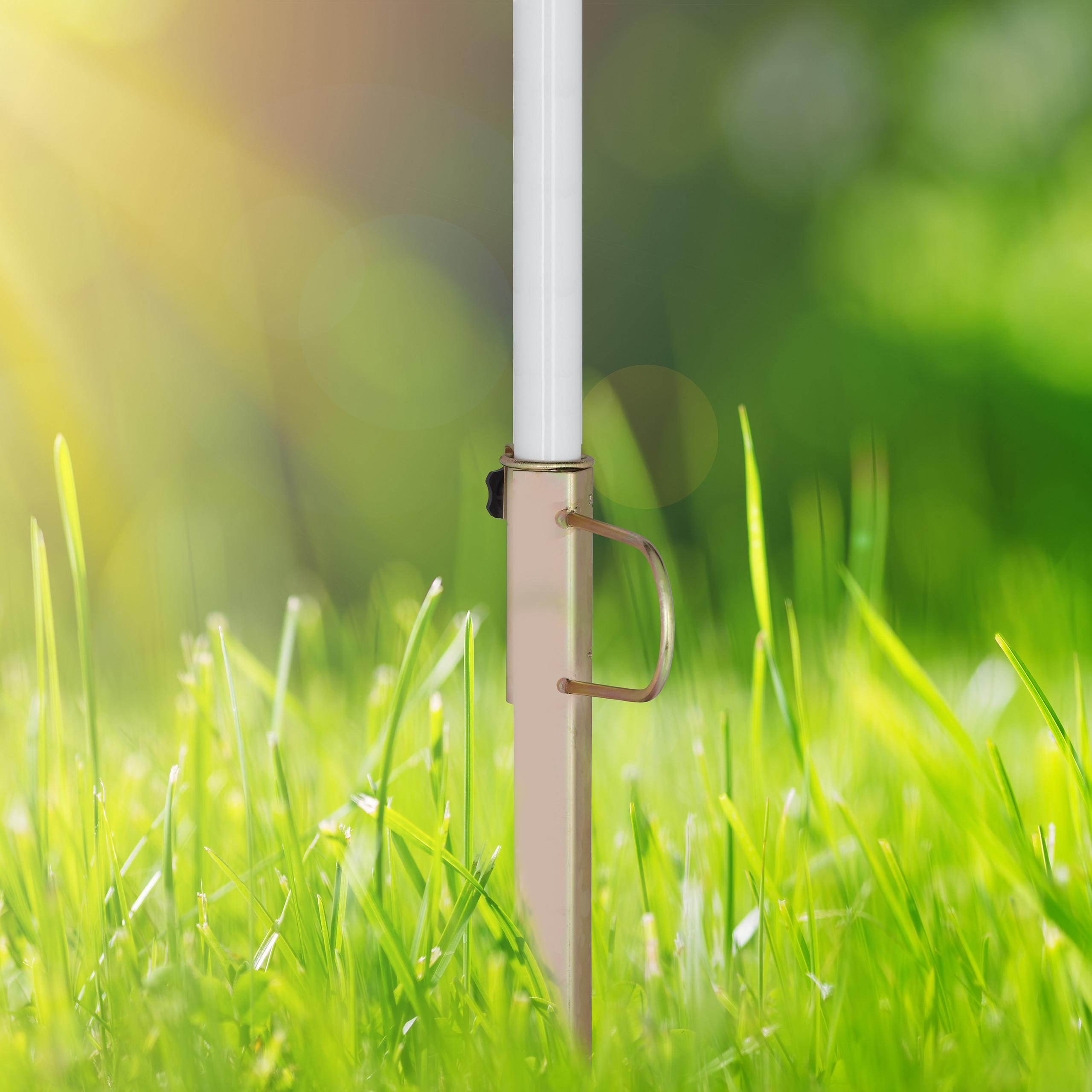 Ein weißer Mast mit einem Metallhalter im grünen Gras vor verschwommenem Hintergrund.