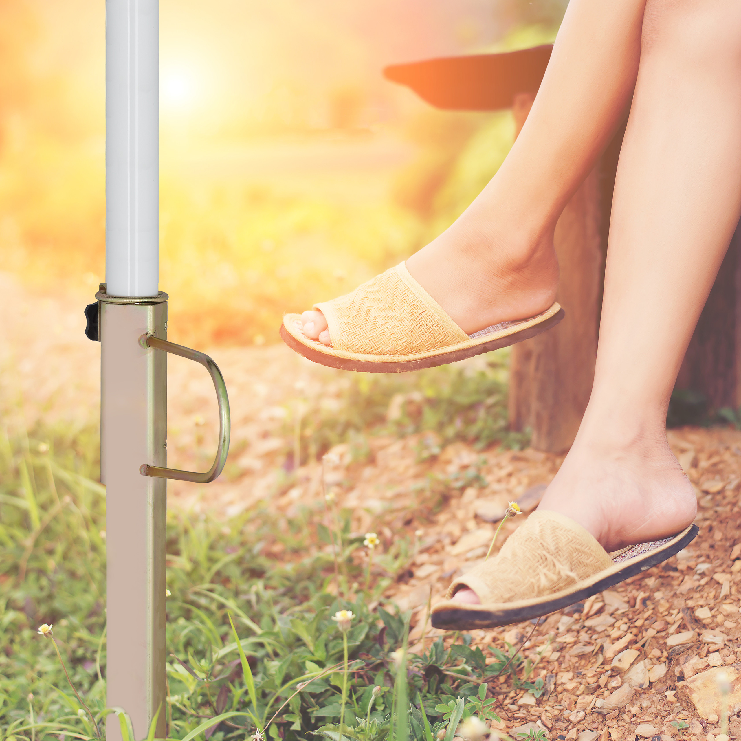 Eine Frau in Sandalen sitzt im Sonnenlicht auf einer Holzbank.