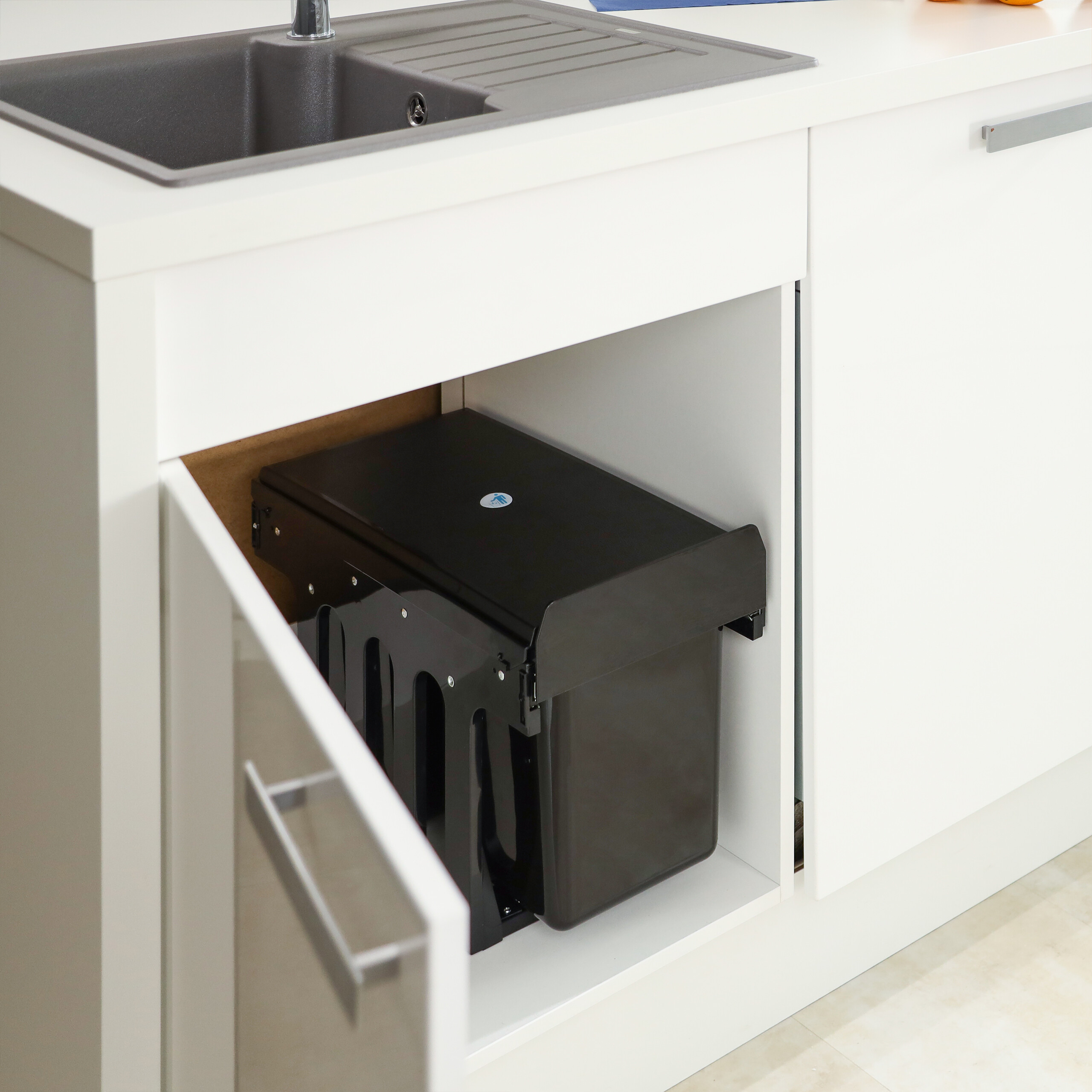 Ein schwarzer Einbau-Mülleimer unter der Küchenspüle, die Schranktür ist leicht geöffnet.