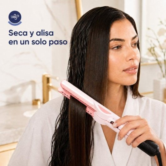 Una donna usa una piastra per capelli rosa sui capelli umidi in un bagno luminoso.