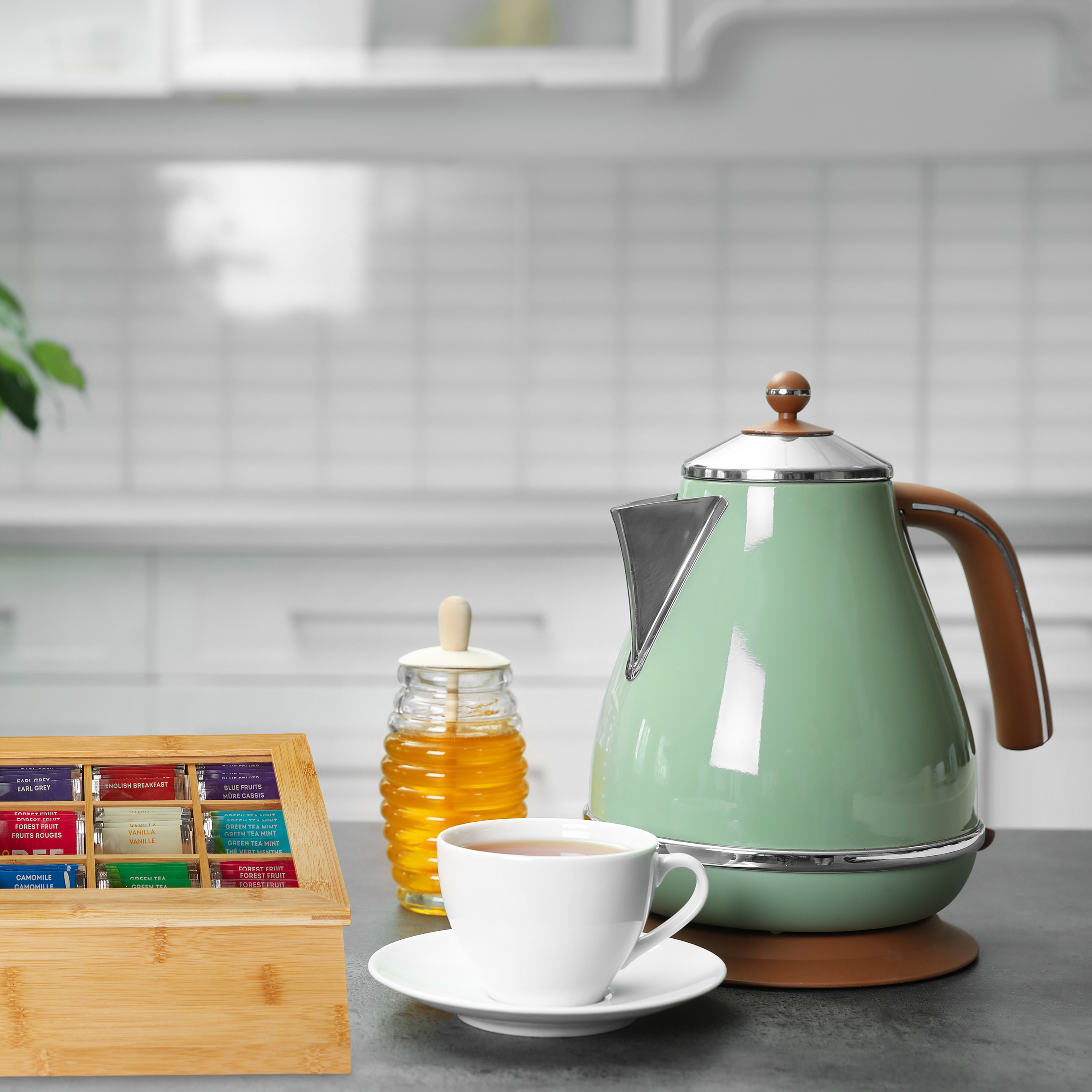 Grüner Wasserkocher, eine Teetasse mit Untertasse, ein Honigglas und eine Teebox auf dem Küchentisch.
