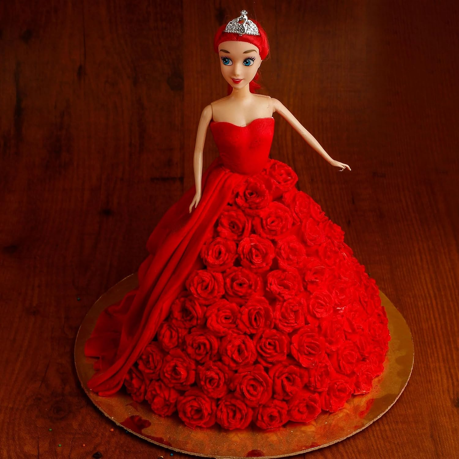 Eine Puppe in einem roten Kleid aus essbaren Rosen und einer kleinen Krone auf dem braunen Holztisch.