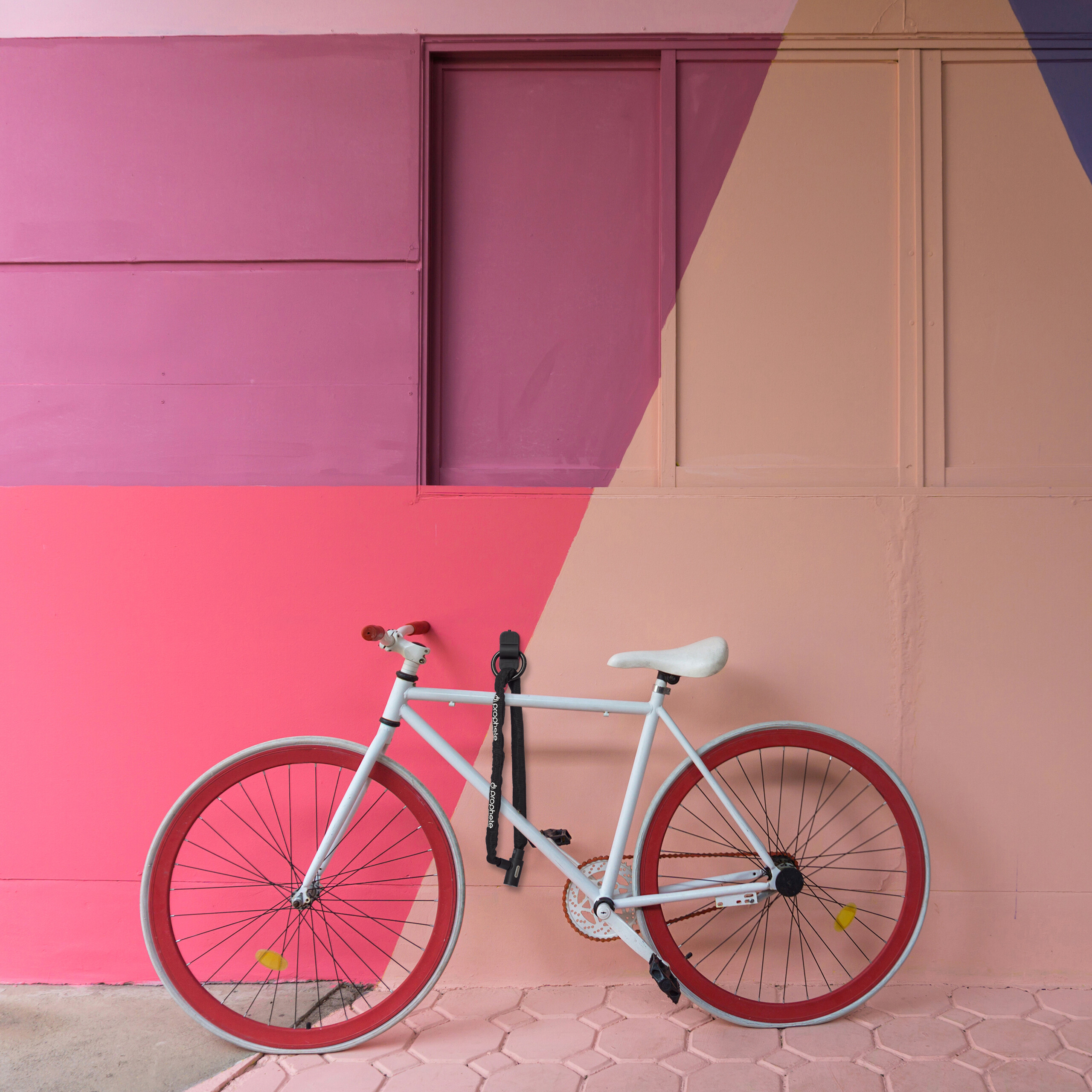 Ein weißes Fahrrad mit roten Felgen steht vor einer rosa und beige gestrichenen Wand.