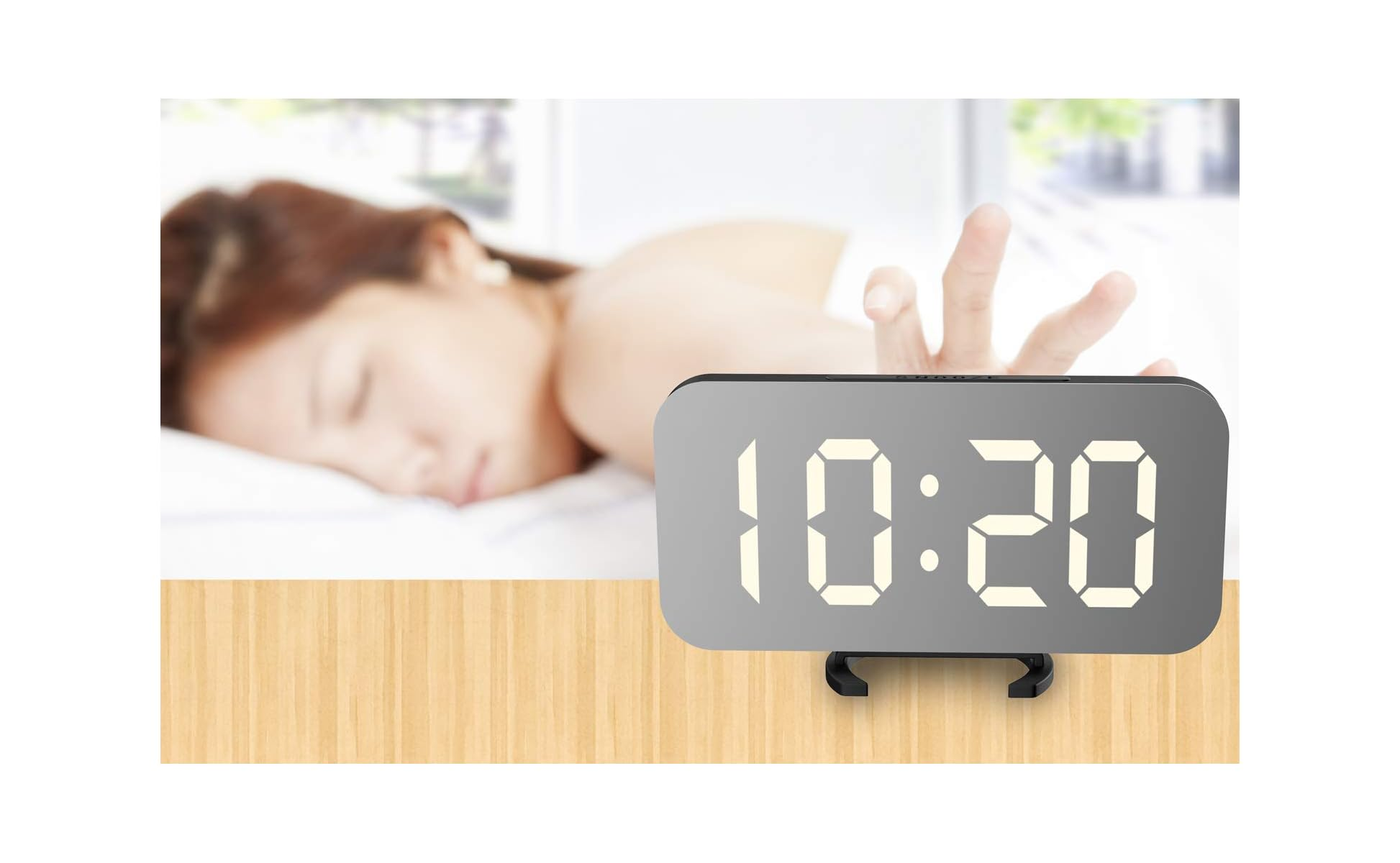 Ein digitaler Wecker auf einem Tisch zeigt 10:20 Uhr. Im Hintergrund schläft eine Person mit ausgestreckter Hand.