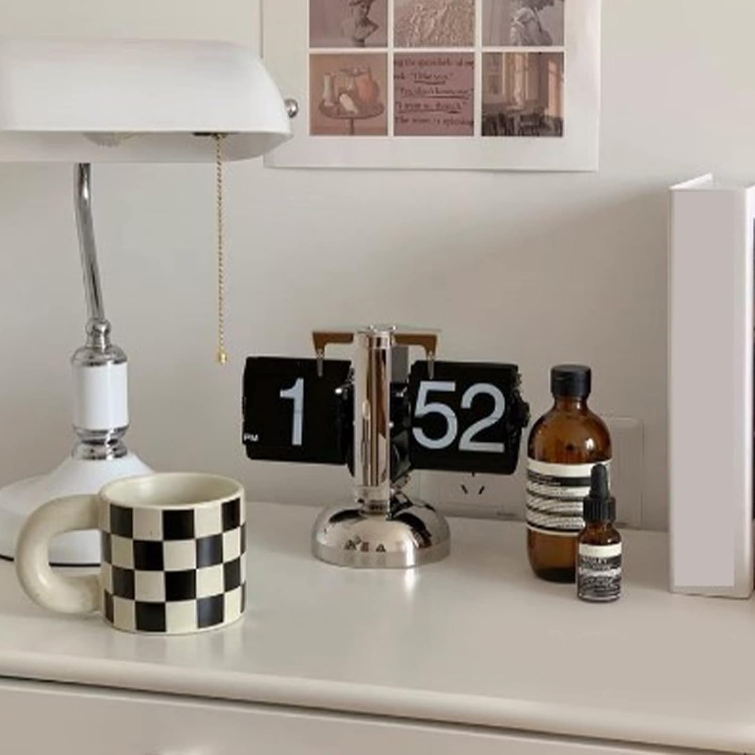 Ein Schreibtisch mit weißer Lampe, karierter Tasse, Klappzahlenuhr auf 1:52 und braunen Flaschen.