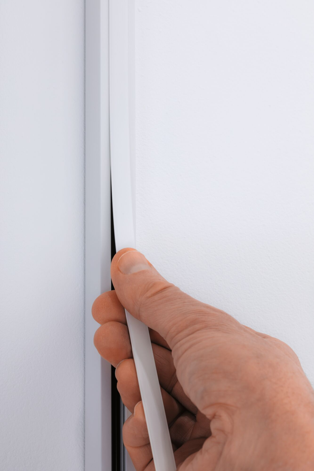 Eine Hand zieht eine weiße Dichtung in einen Fensterrahmen.