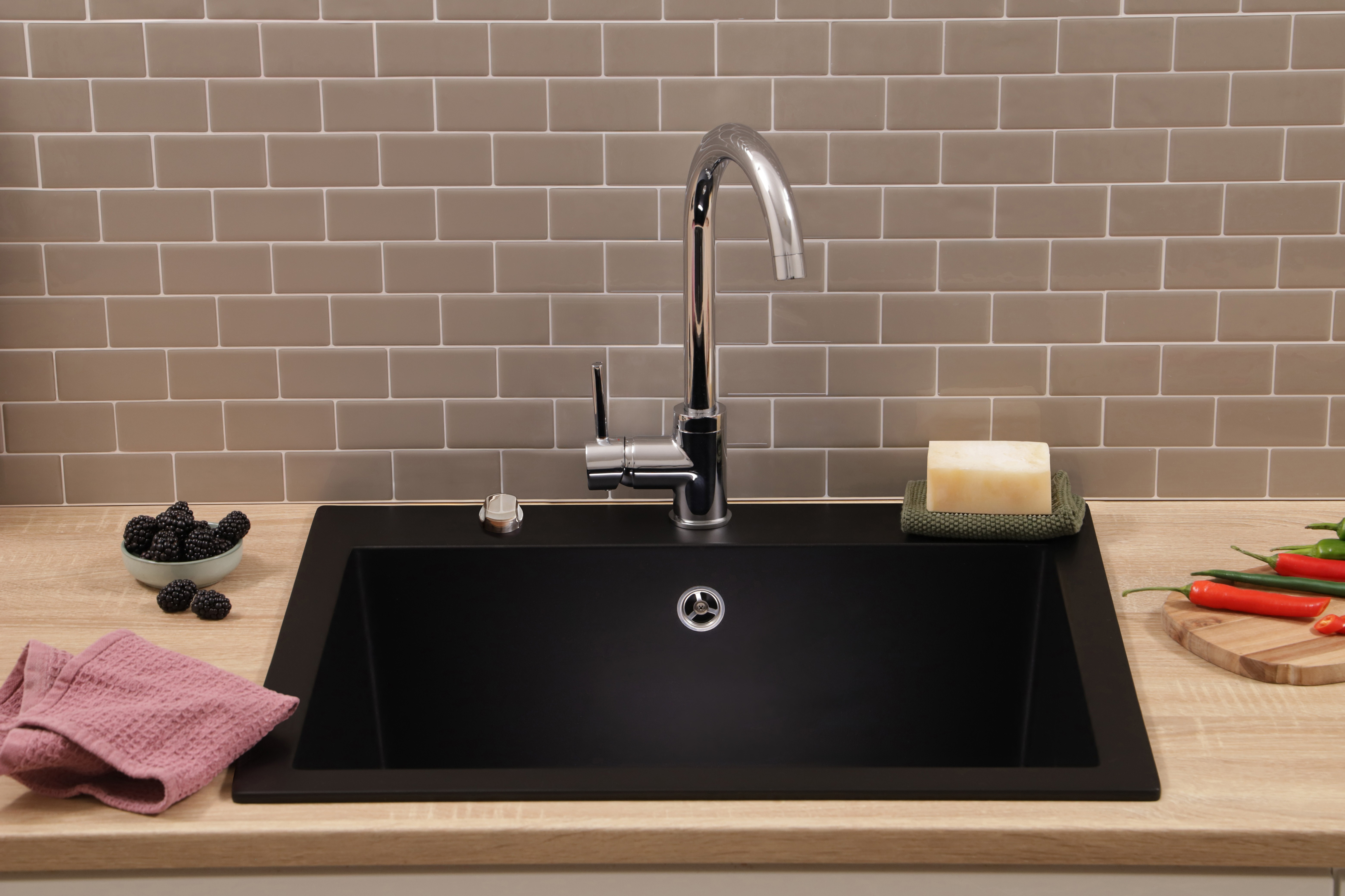 Eine schwarze Küchenspüle mit Chromarmatur auf Holzarbeitsplatte und grauen Fliesen im Hintergrund.