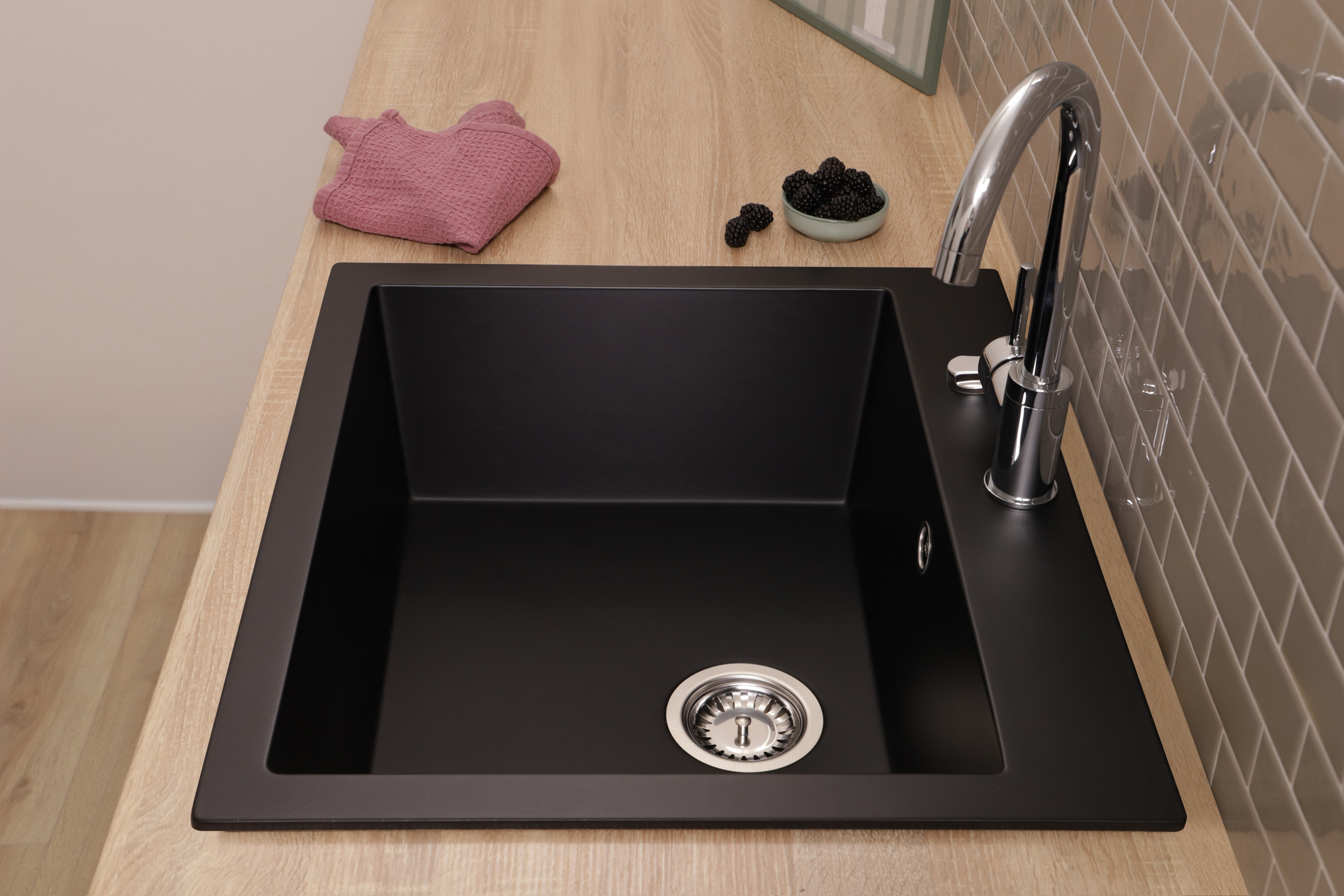 Eine schwarze Küchenspüle mit Chromarmatur auf einer Holzarbeitsplatte und graue Fliesen an der Wand.