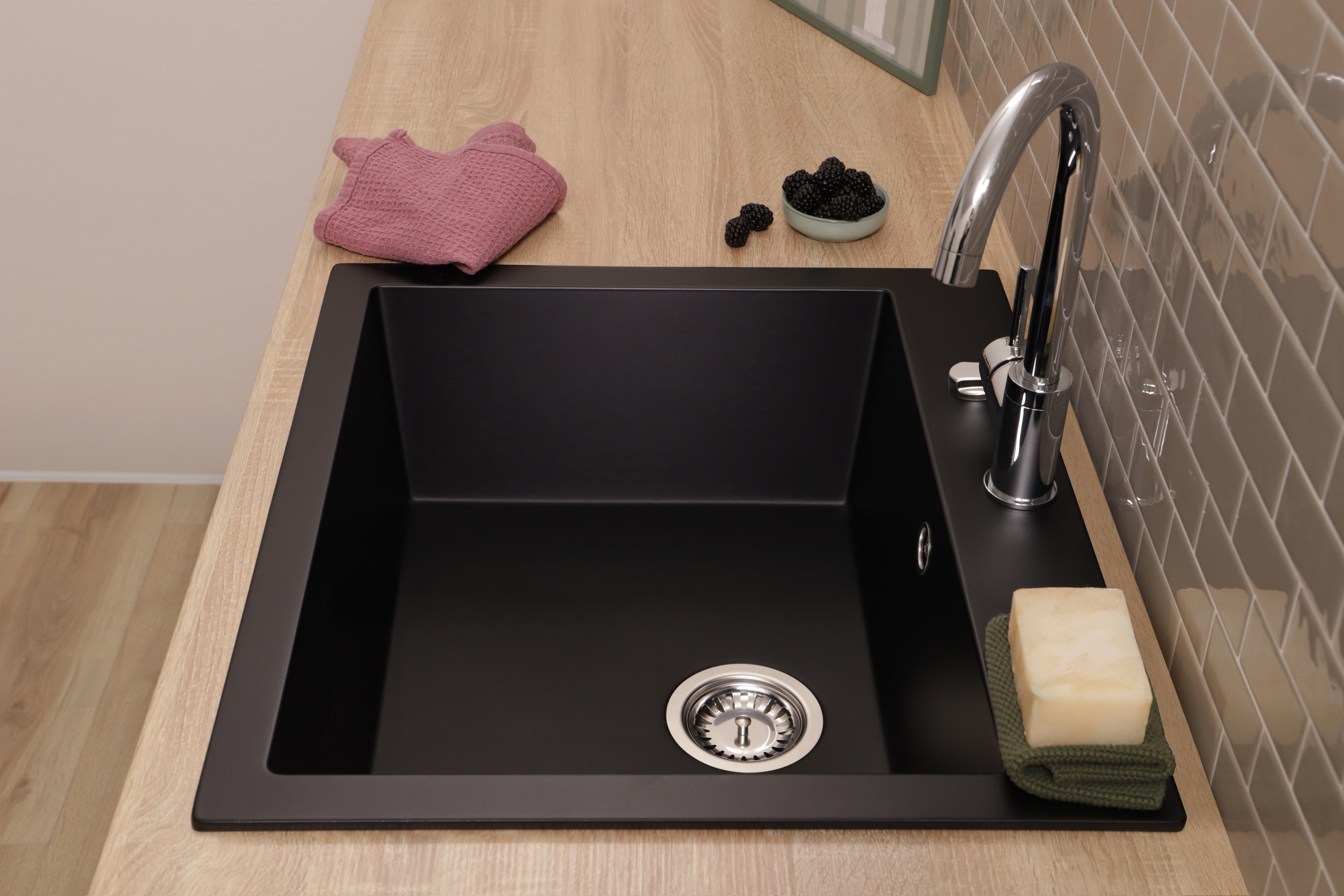 Ein schwarzes Spülbecken mit Chromarmatur auf Holzplatte, daneben eine Schale Brombeeren und ein Seifenstück.