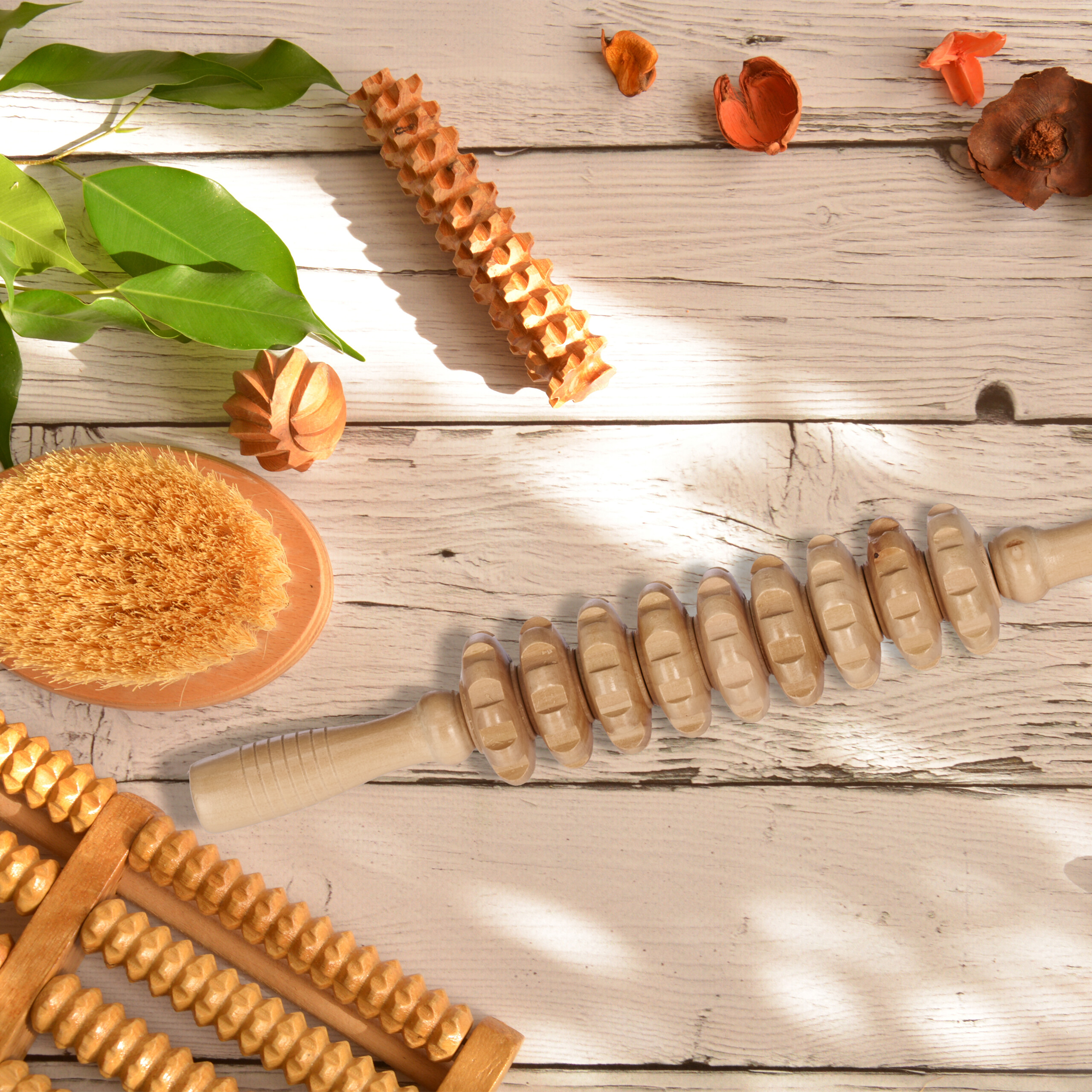 Holzmassagegeräte, eine Bürste und grüne Blätter auf einem Holztisch.