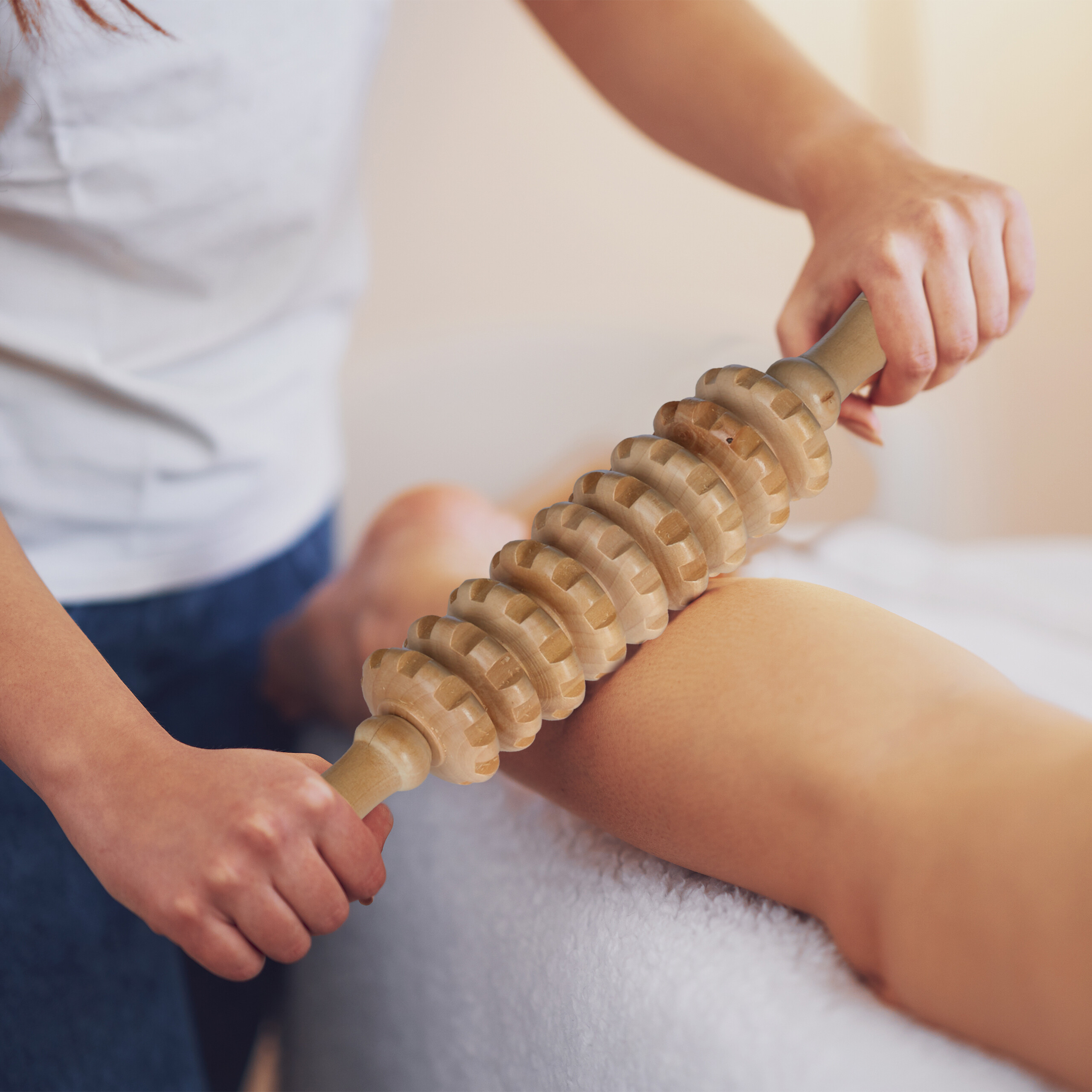 Eine Frau gibt einer anderen Person mit einer strukturierten Holzwalze eine Massage am Bein.