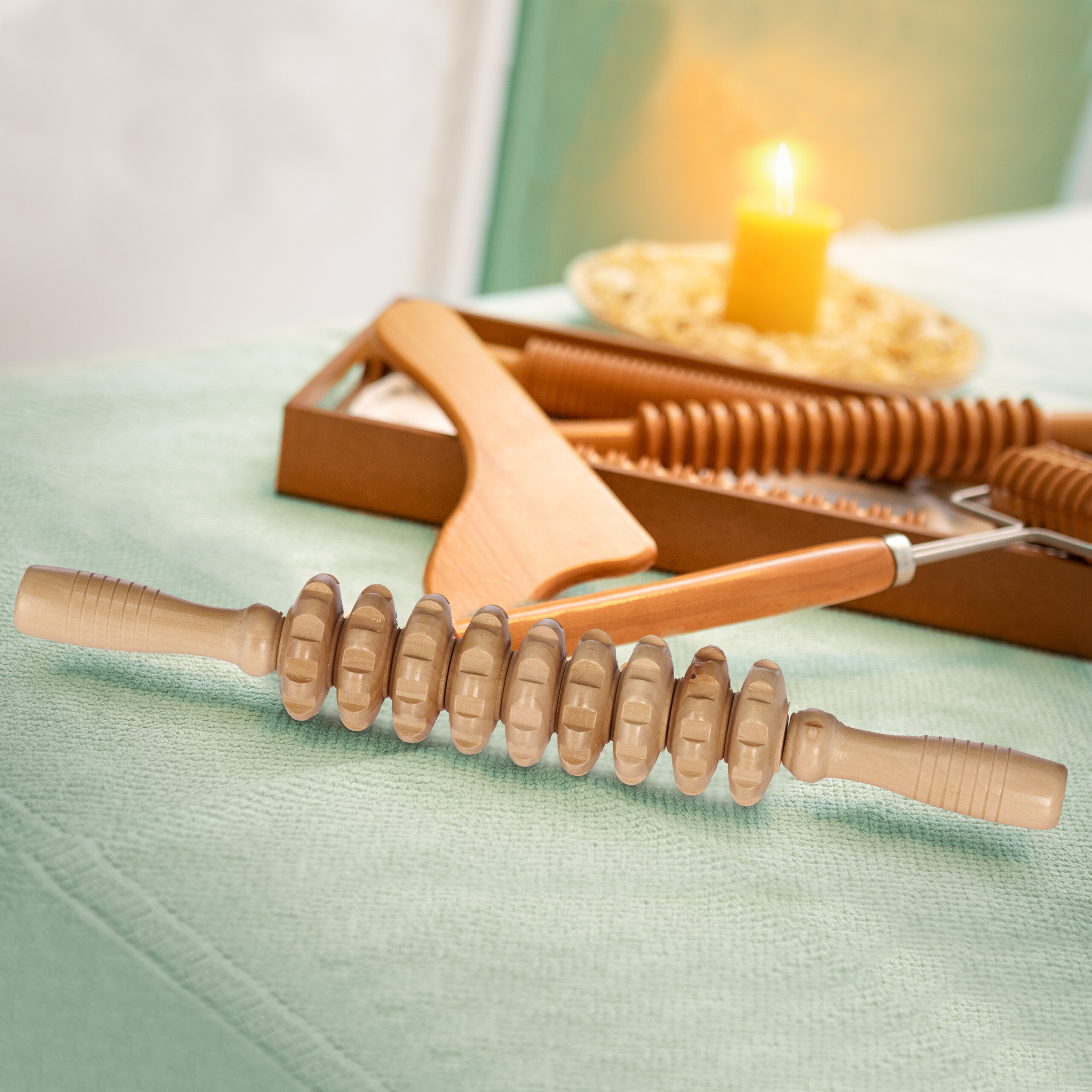 Holzmassagegeräte für die Maderotherapie liegen auf einem grünen Tuch, im Hintergrund brennt eine gelbe Kerze.