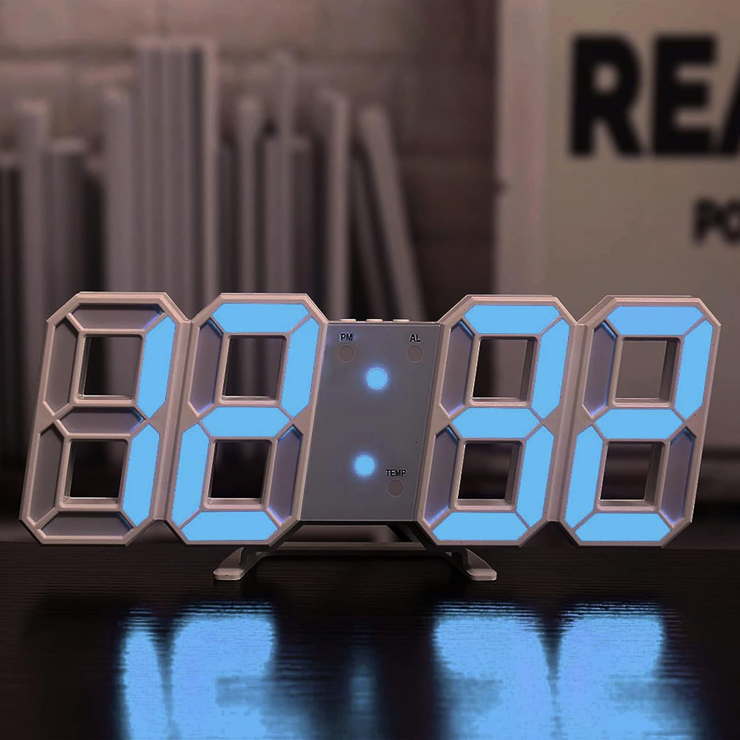 Eine weiße digitale Tischuhr mit leuchtend blauen LED-Ziffern steht auf einer dunklen Oberfläche vor einem unscharfen Hintergrund.