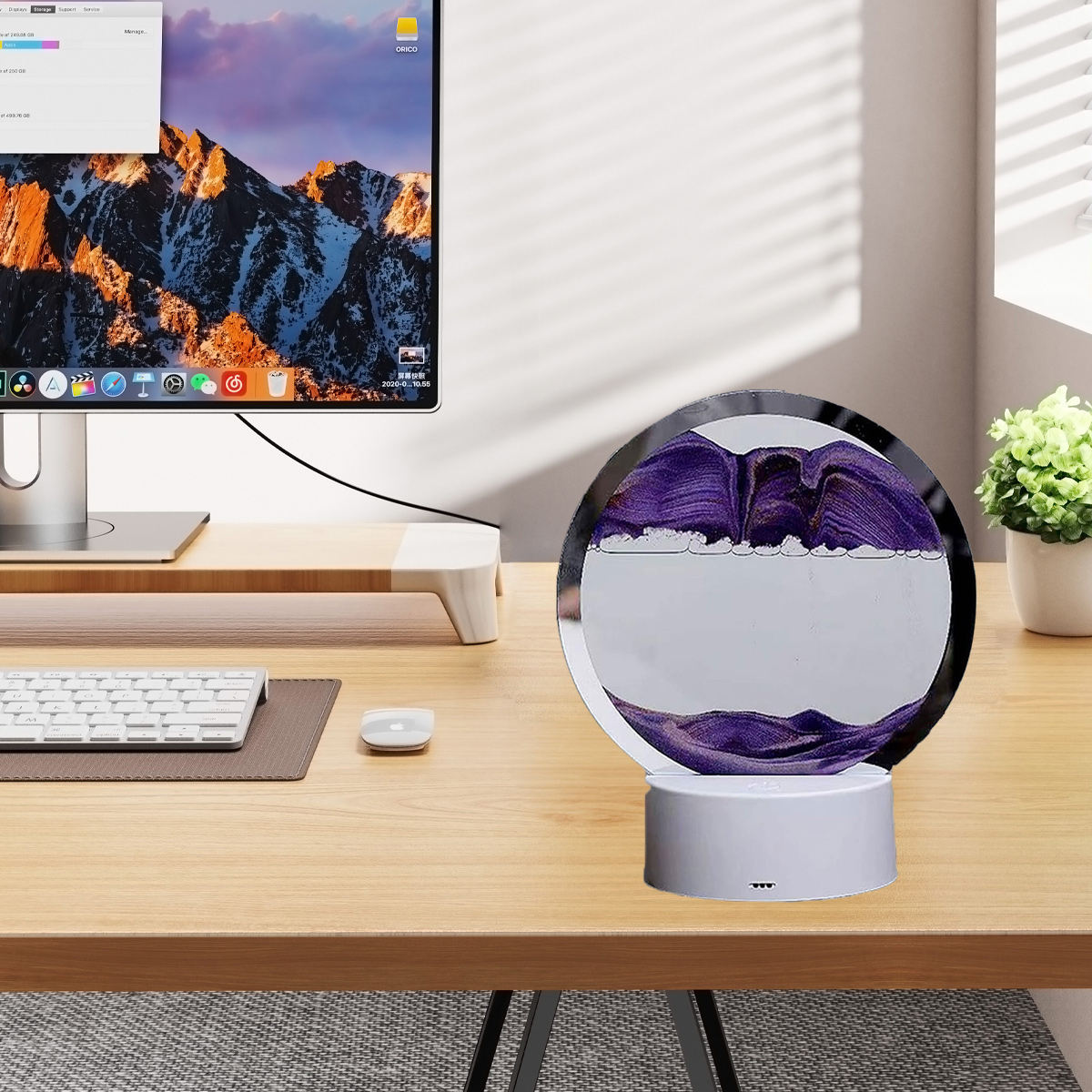 Eine runde, violette Sanduhr auf einem Holztisch, neben einem Computer und einer Pflanze.