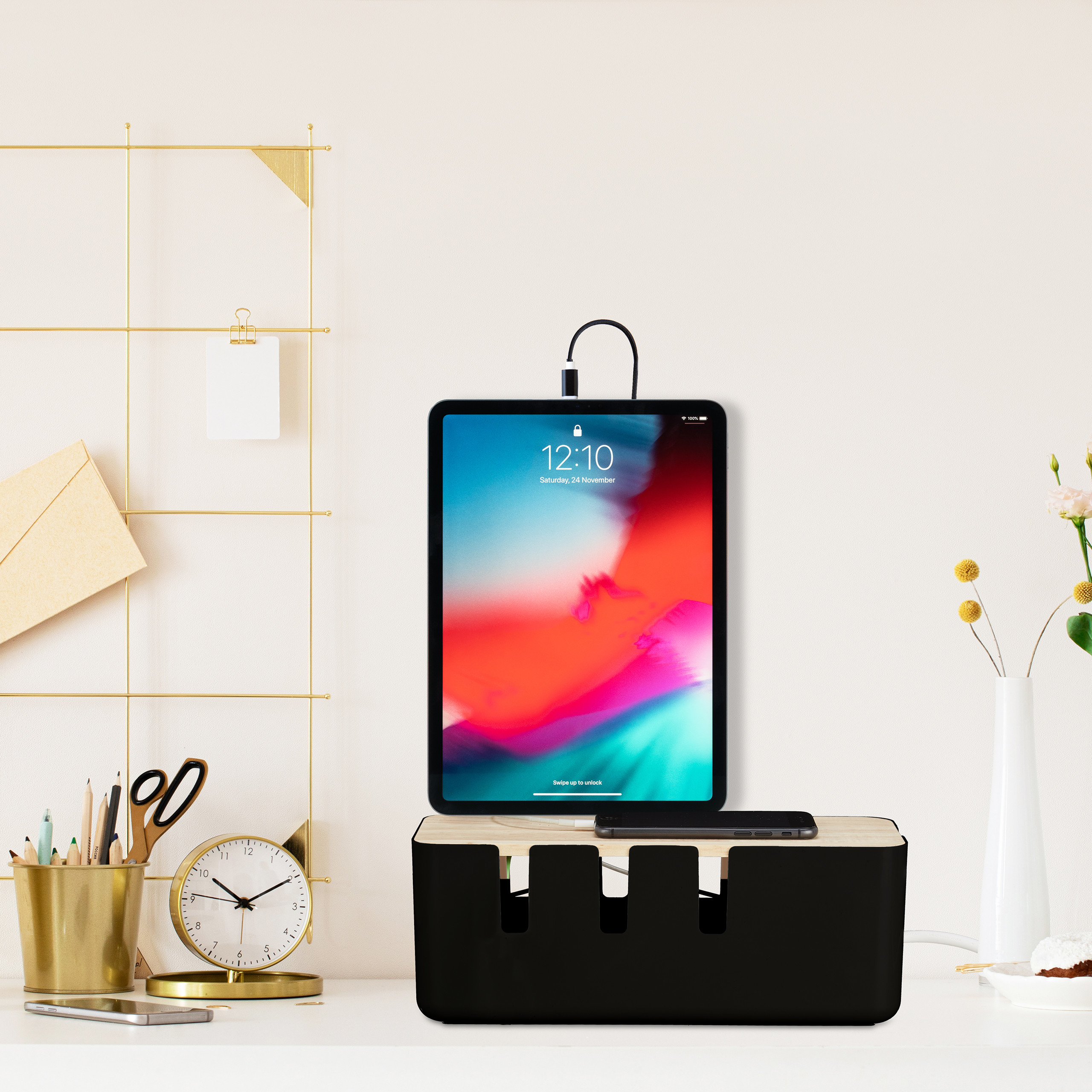 Ein Tablet und Smartphone laden auf einer schwarzen Kabelbox auf einem weißen Schreibtisch.